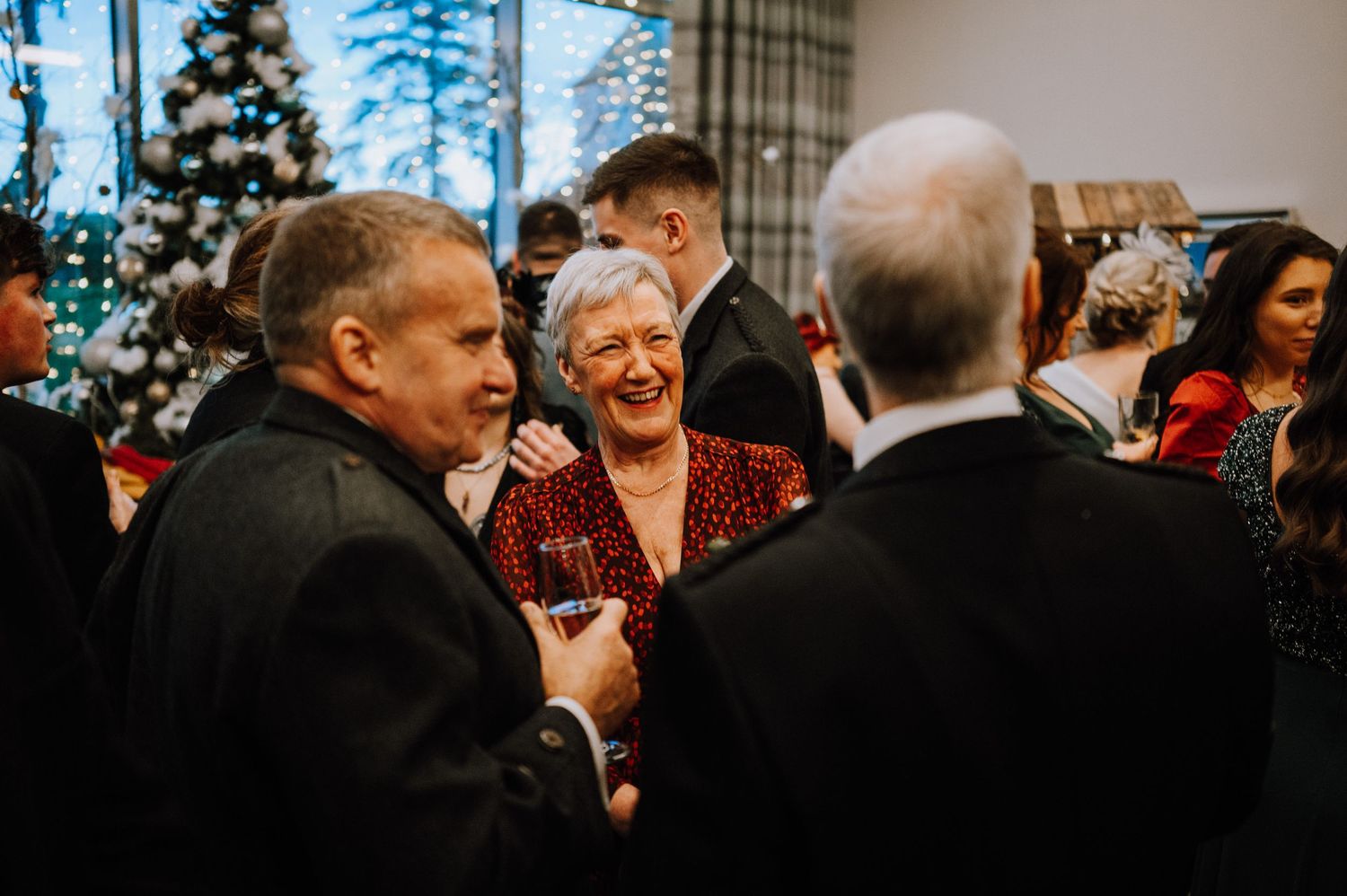 Party guests engage in lively conversation near a decorated Christmas tree.