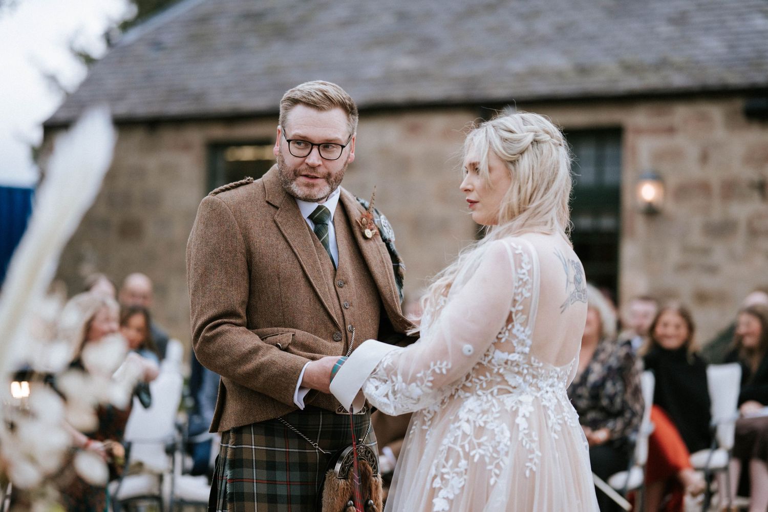 A romantic wedding ceremony takes place against the backdrop of a historic stone building.