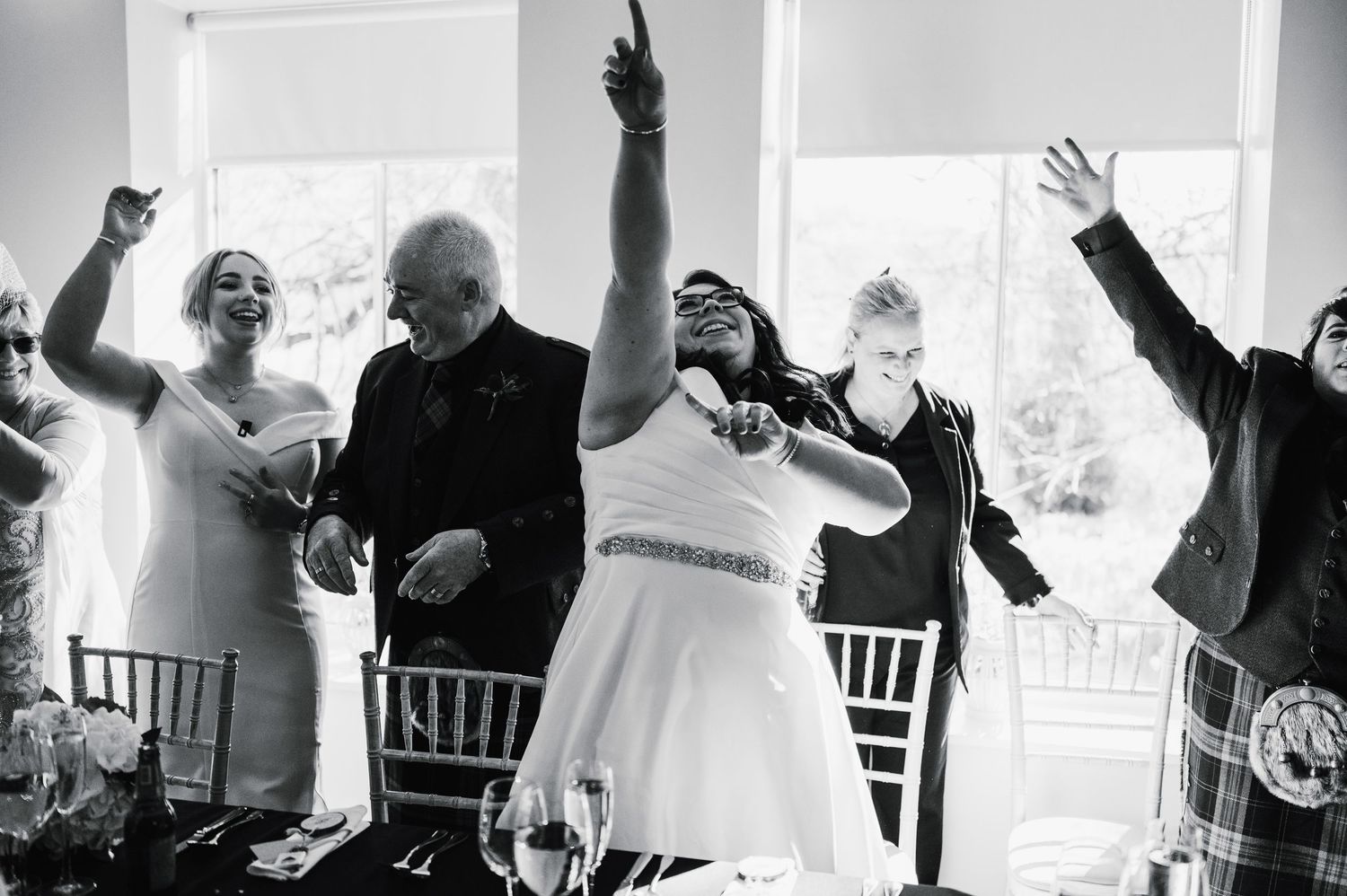 Logie House Wedding Photography. Wedding celebration with people dancing joyfully in a bright indoor venue.