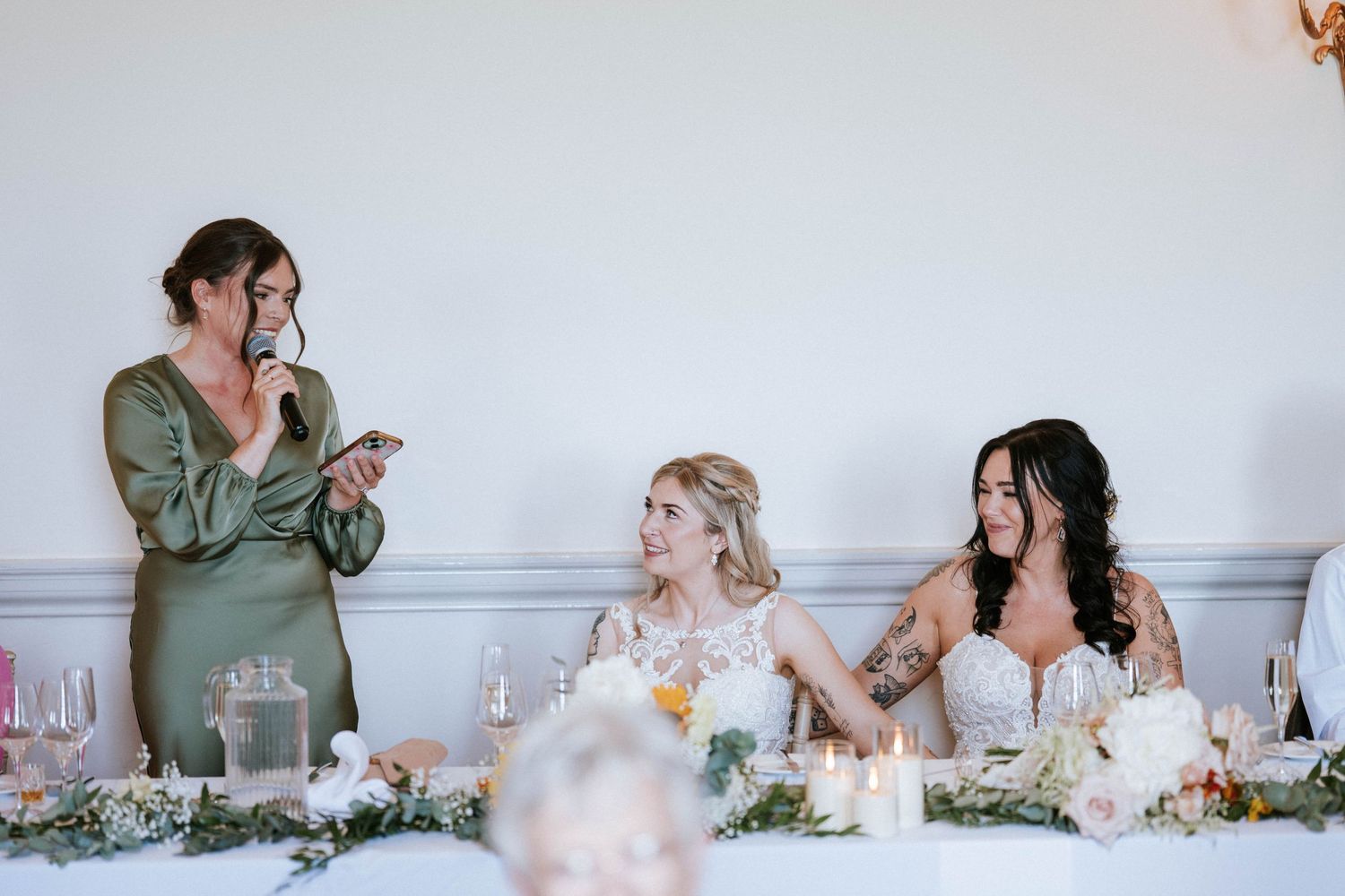 Fasque Castle Wedding Photography. Wedding party members seated at a decorated head table share joyful moments during reception.