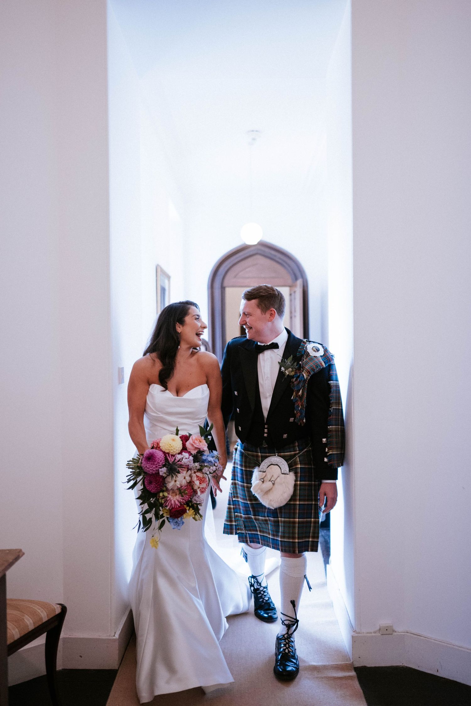 Newlyweds walking through arched church hallway with Scottish kilt and white wedding dress.