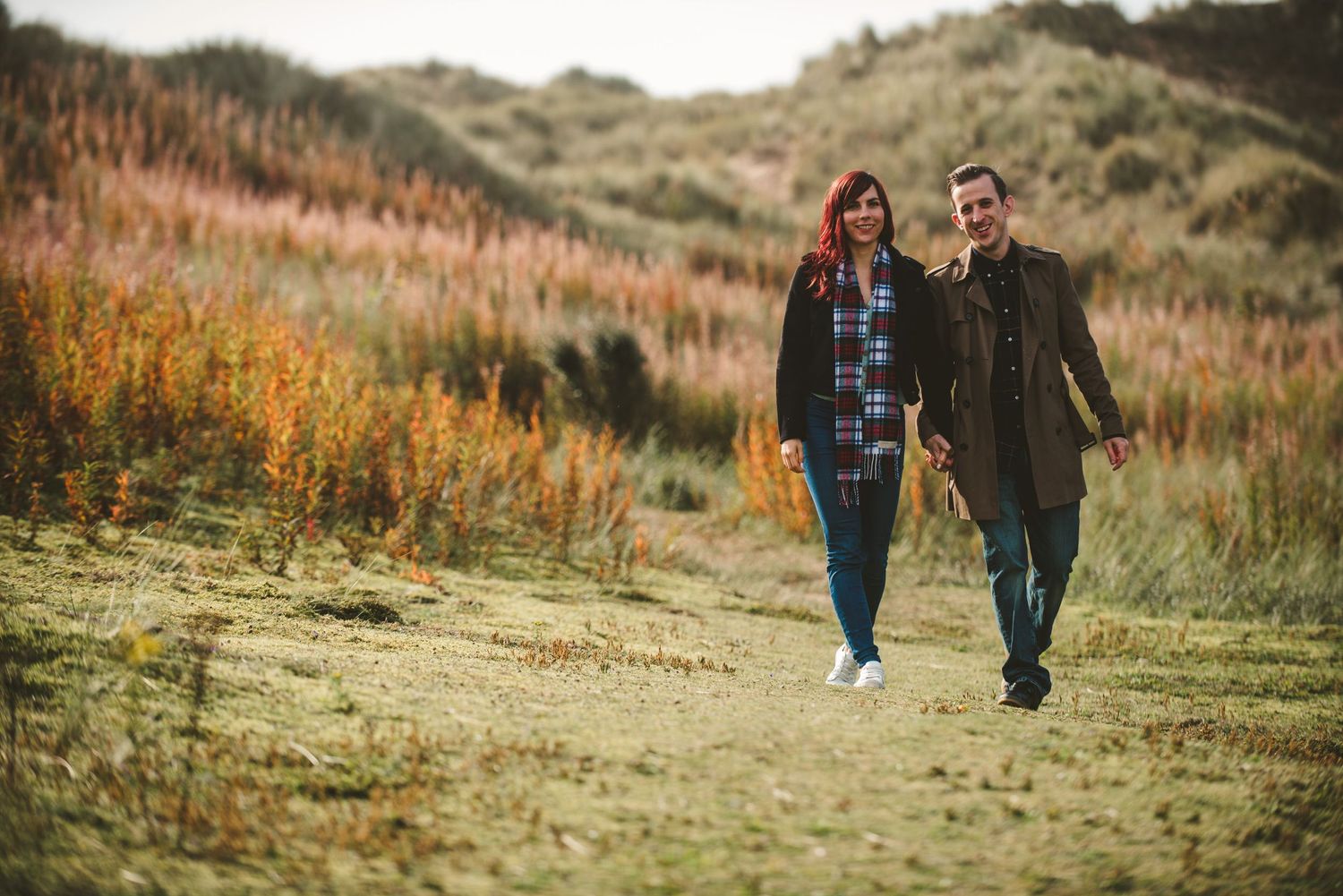 A happy couple strolling along a path with golden fall grasses in the background.