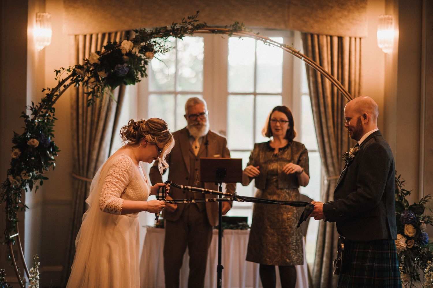Wedding ceremony under a decorated arch with couples exchanging rings.