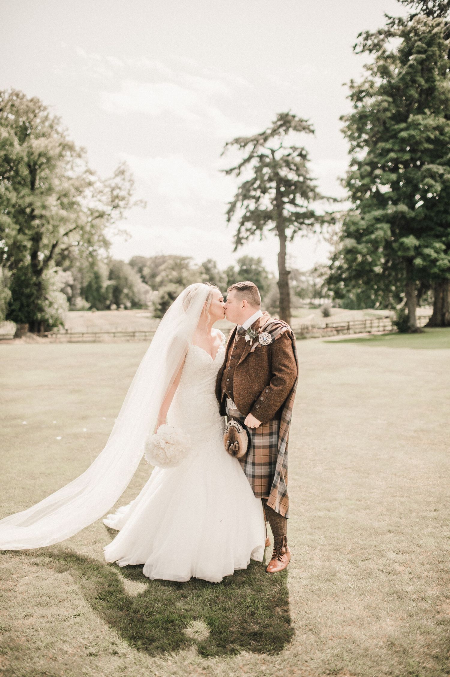 Wedding couple shares intimate moment on lawn with bride's veil flowing in the wind.