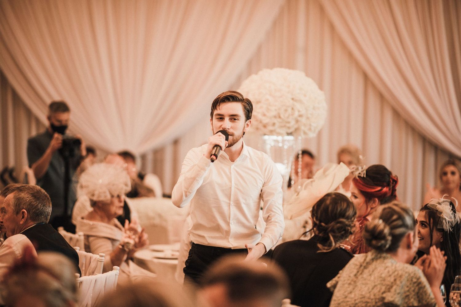 Guest delivers heartfelt speech during elegant wedding reception with white decor.