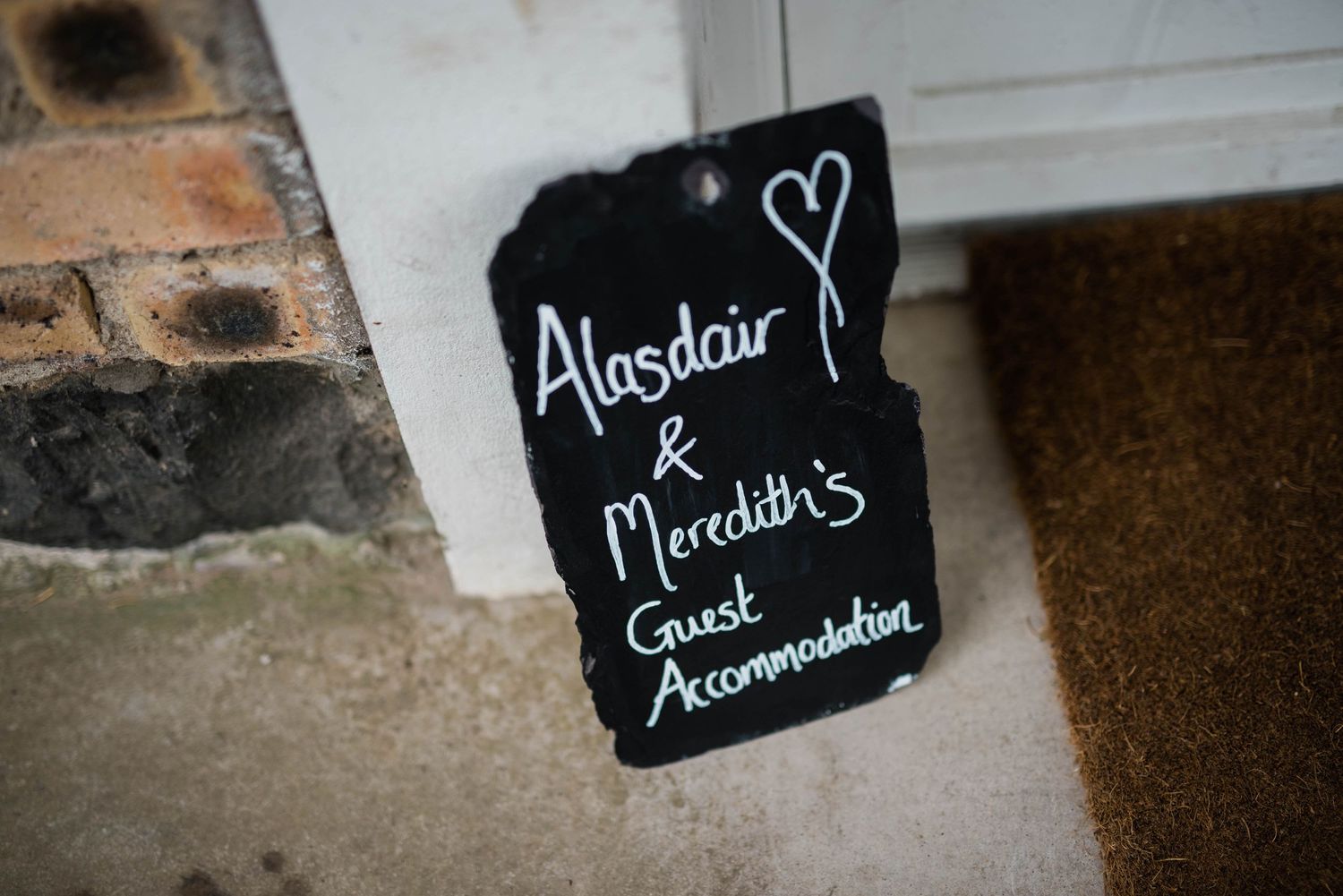 Rustic chalkboard sign with handwritten wedding accommodation details and heart drawing.
