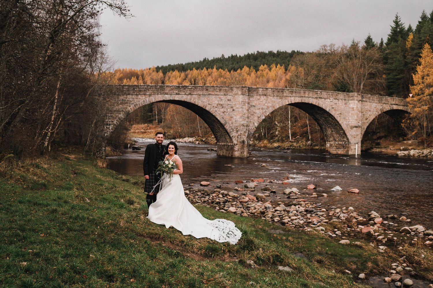 Wedding portrait with dramatic stone bridge and autumn foliage in background.