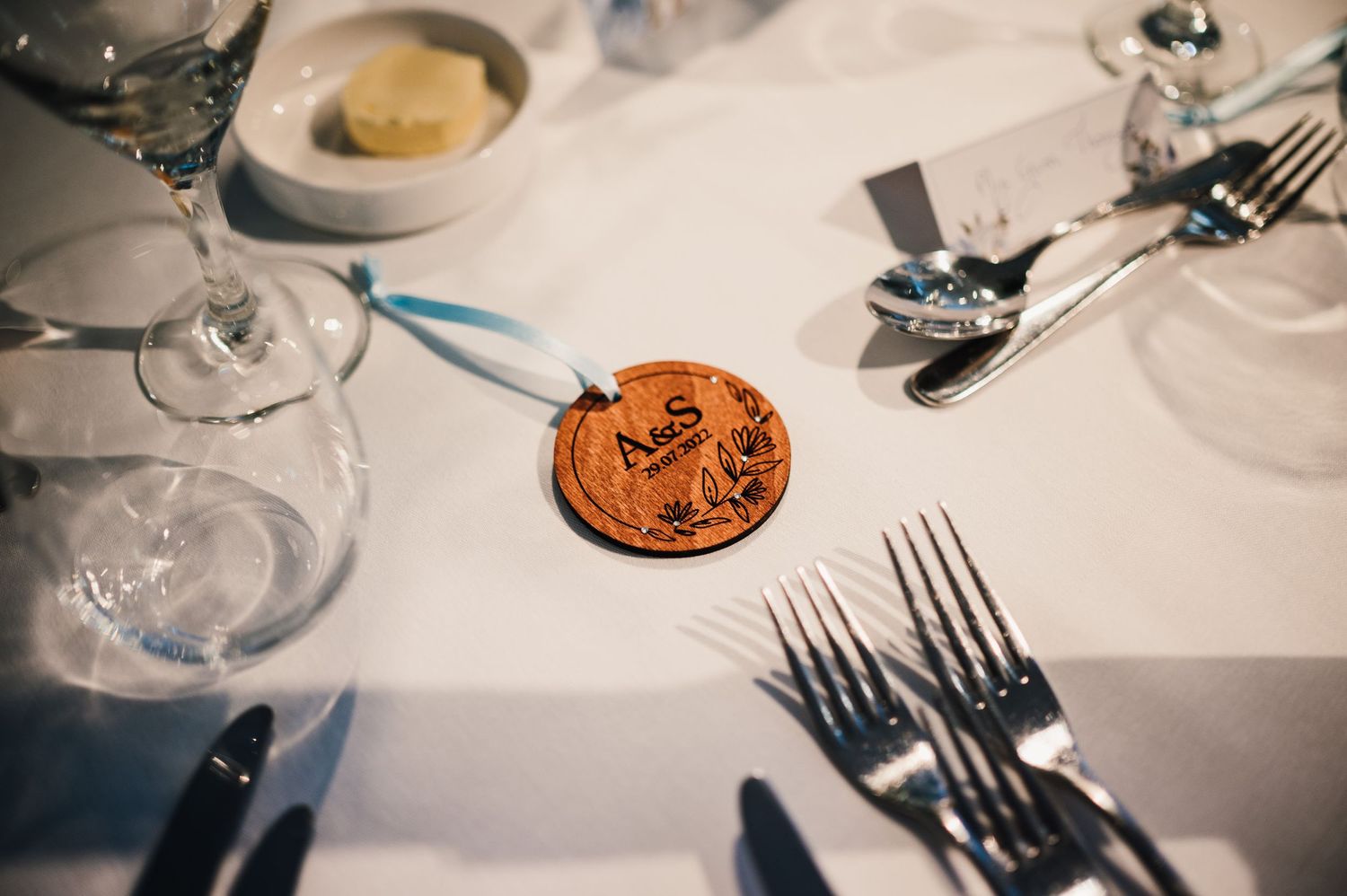 Place setting at wedding reception with decorative wooden coin and formal silverware.