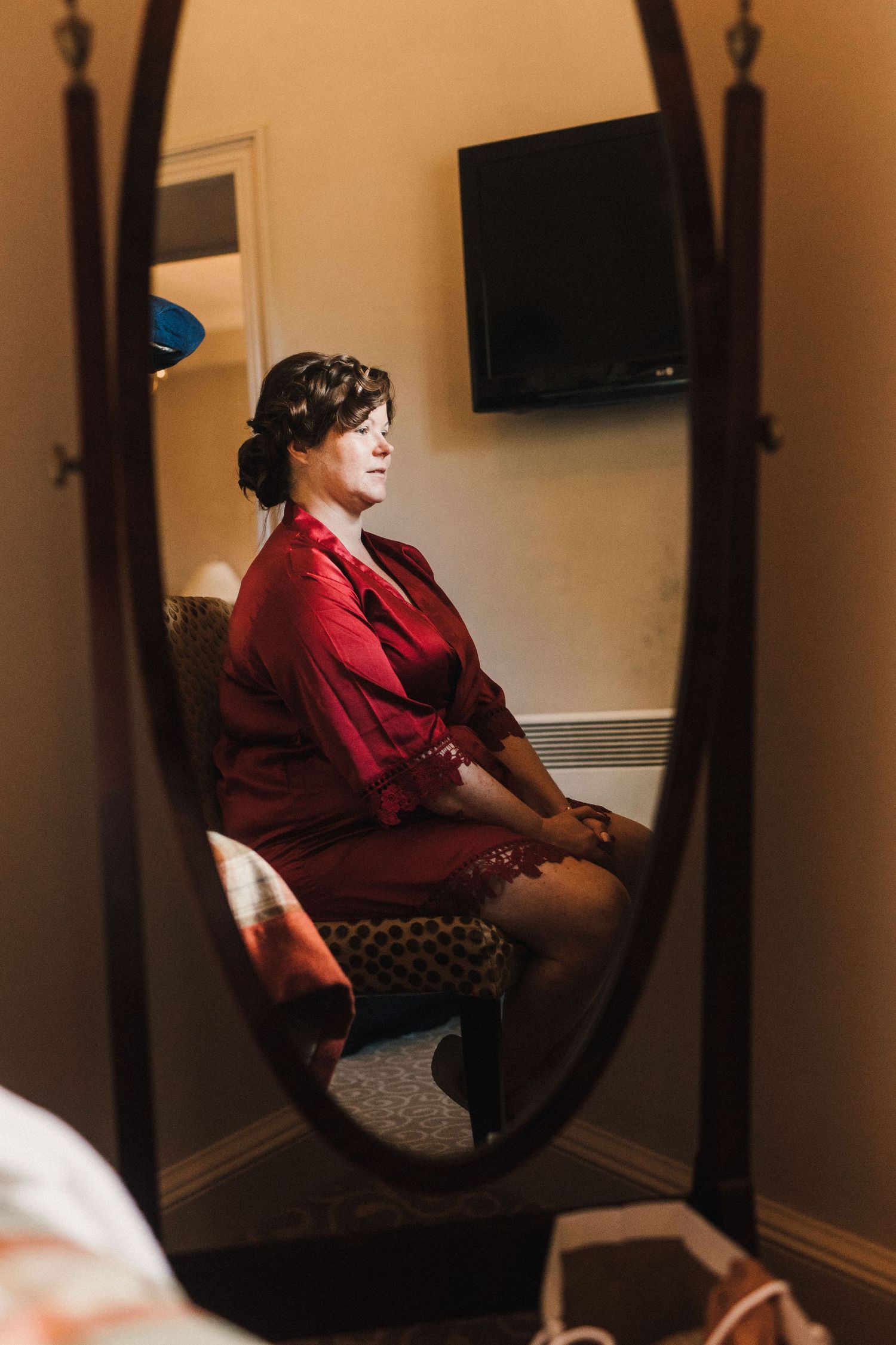 Reflection in ornate mirror shows person in red robe sitting in preparation room.
