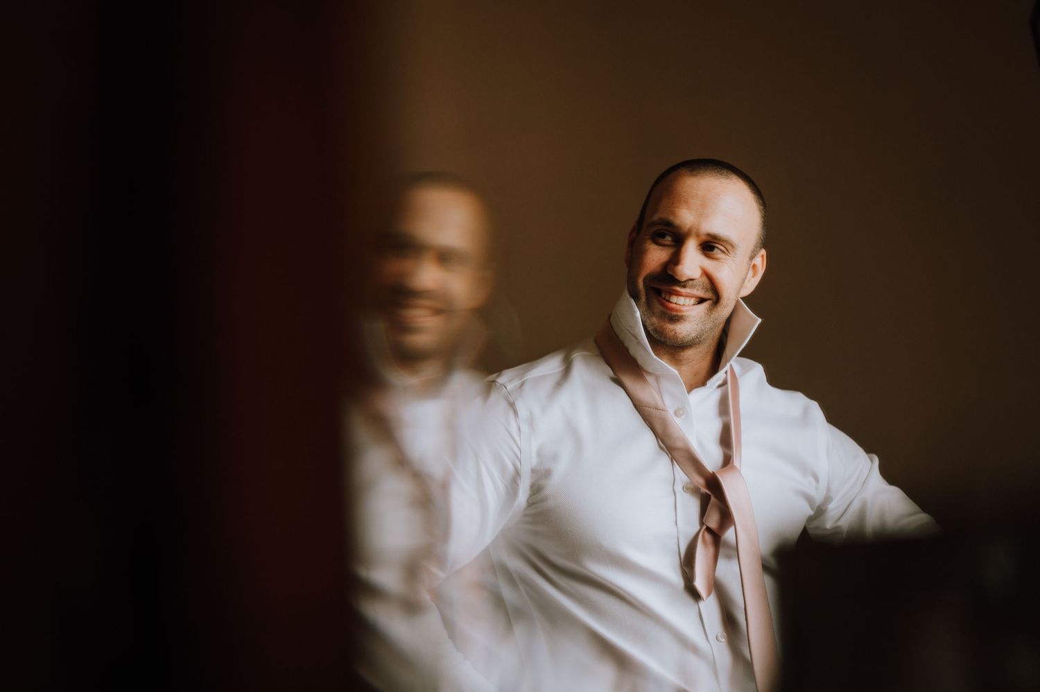 Light-hearted candid portrait in white dress shirt against dark background with reflection.