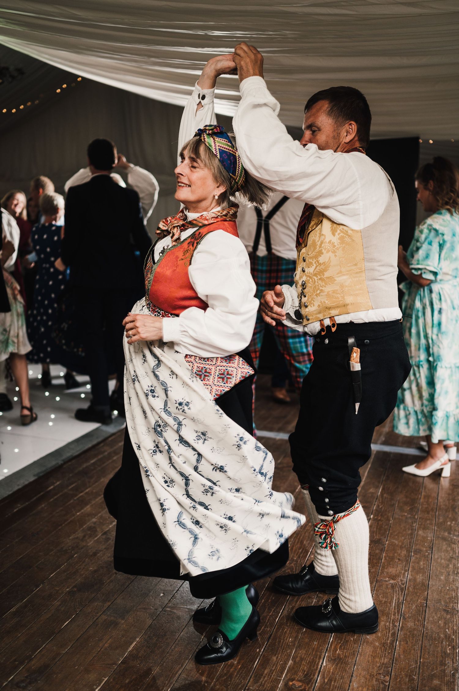 Couple performing traditional folk dance in cultural attire at wedding reception.