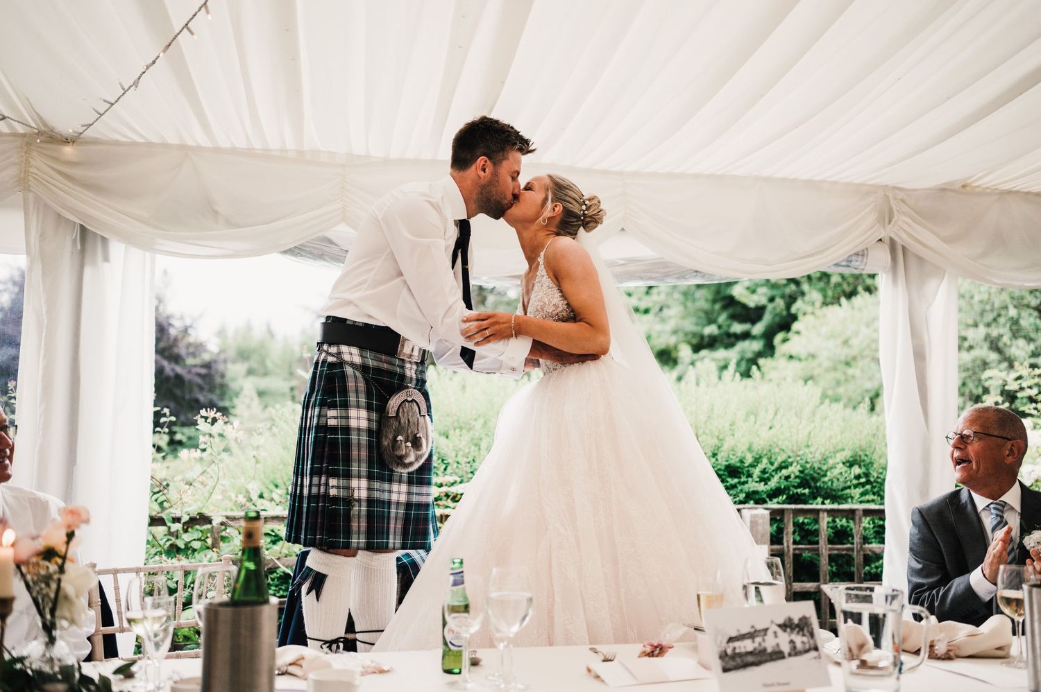 Romantic moment between newlyweds at Scottish wedding reception with traditional kilt attire.