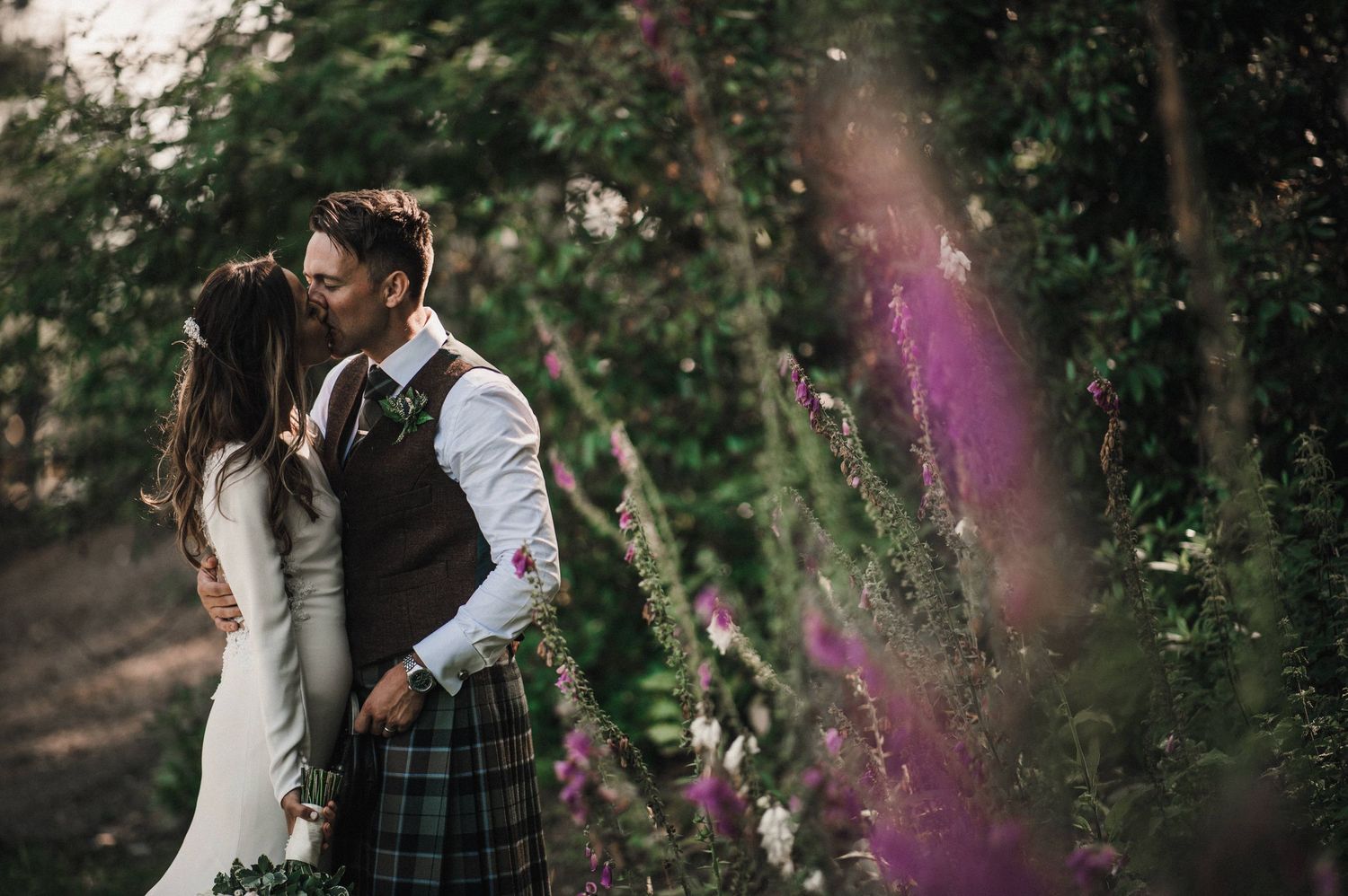 Romantic forest wedding photo with couple in Scottish dress framed by natural foliage.
