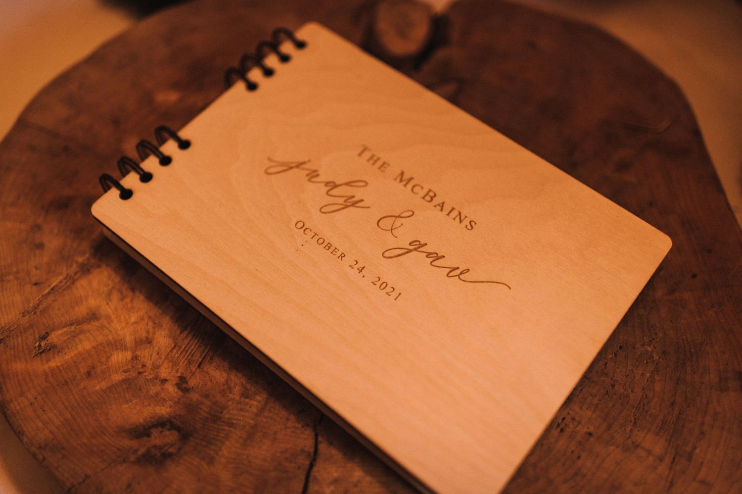 Wedding guestbook with engraved names on wooden surface in warm lighting.