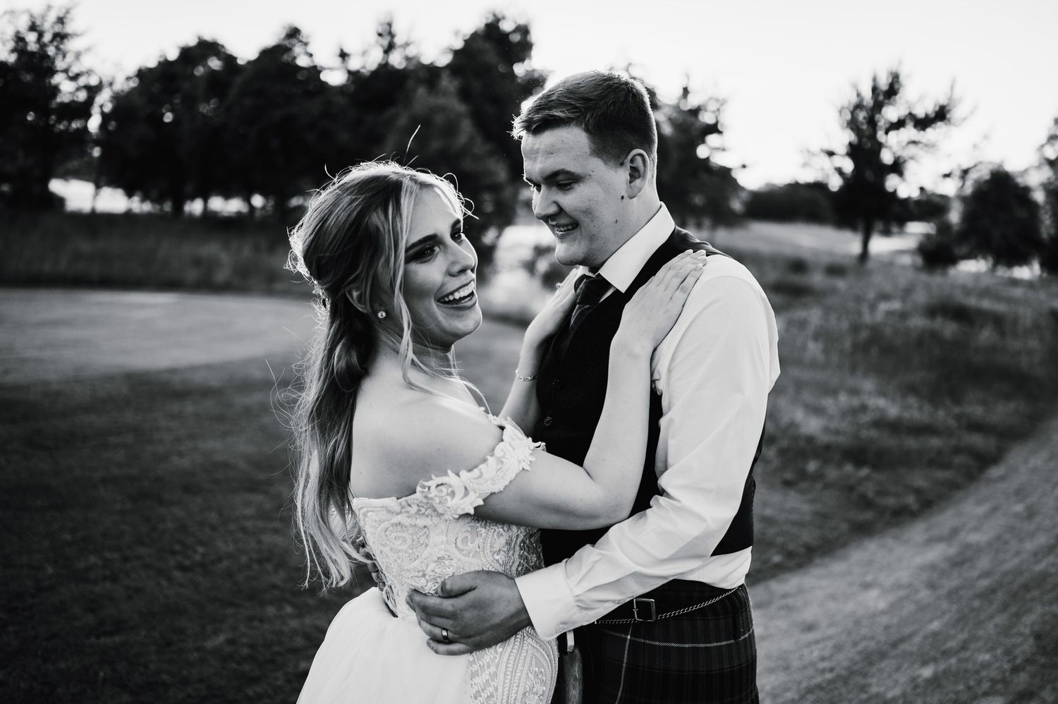 A black and white portrait of a couple in wedding attire sharing an intimate moment outdoors.