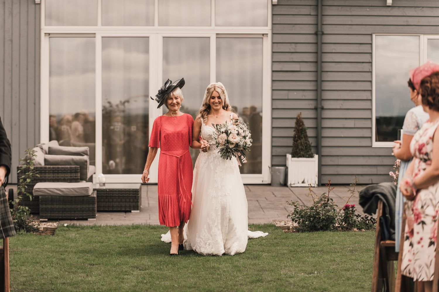 Wedding party members walk along a modern venue's garden path during ceremony.