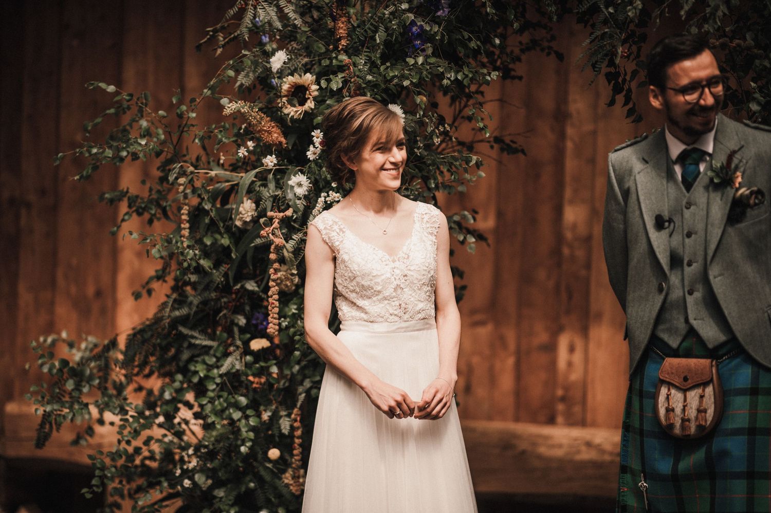 A wedding ceremony scene with Scottish highland dress and floral arch decorations.