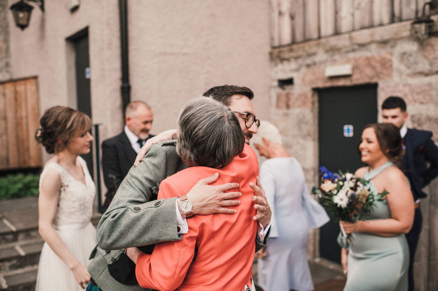 Warm embraces shared during wedding celebrations outside a historic Scottish building.
