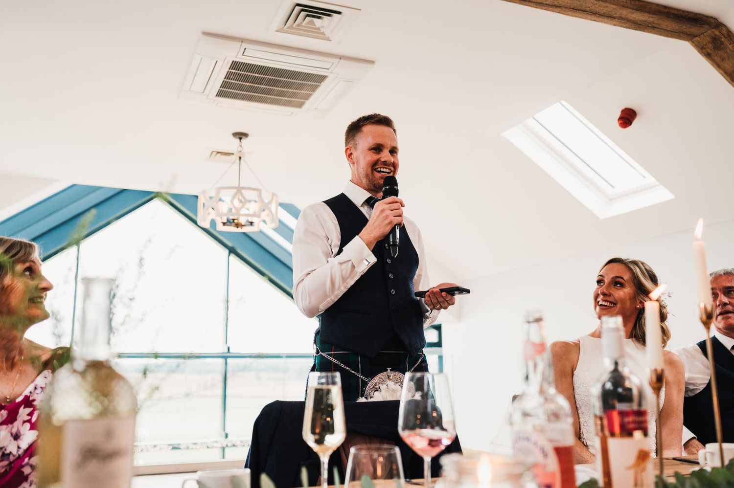 Speaker delivers wedding toast while standing at decorated reception table.