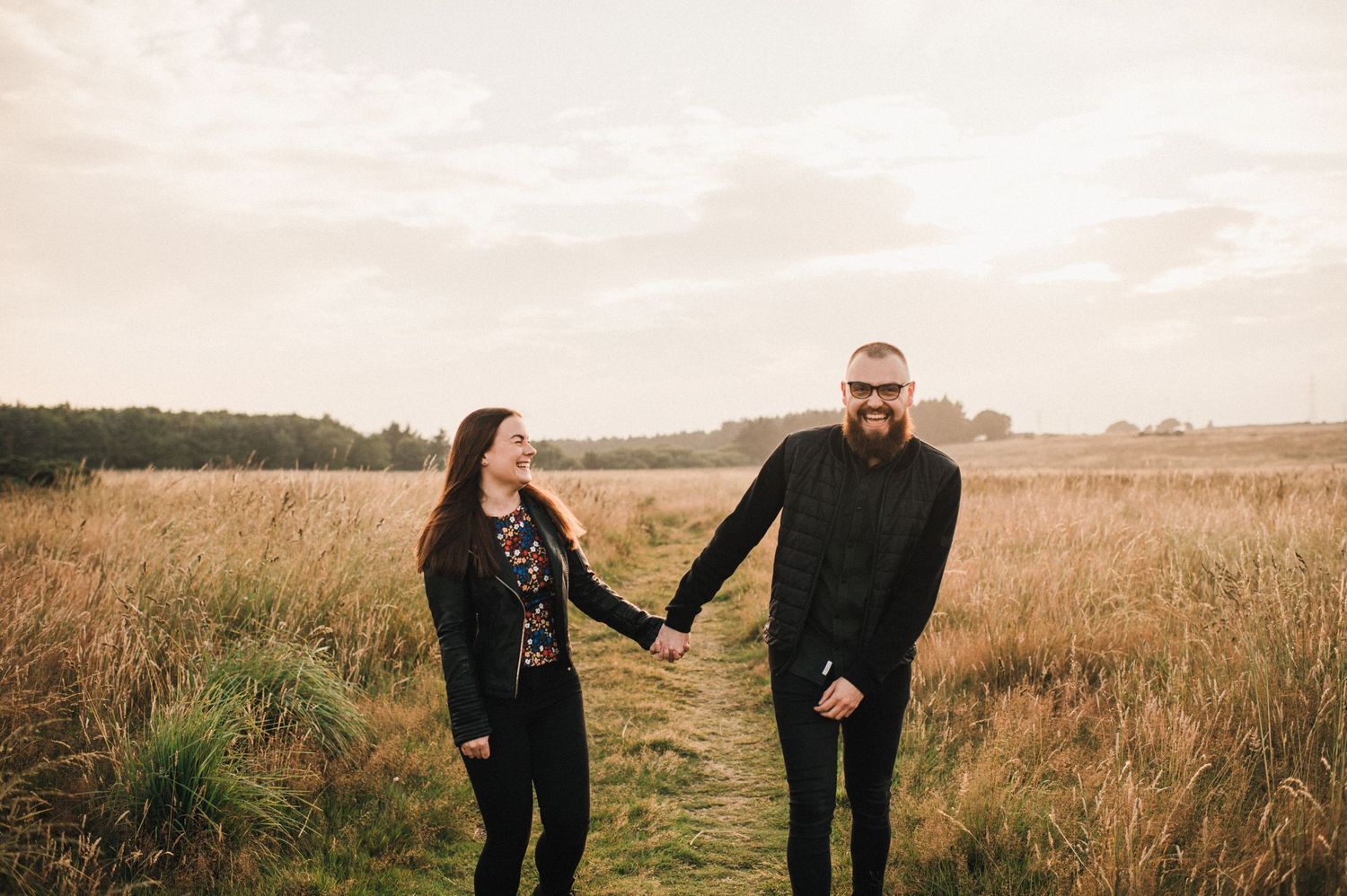 A couple shares a sweet moment while standing together in a serene autumn field at golden hour.