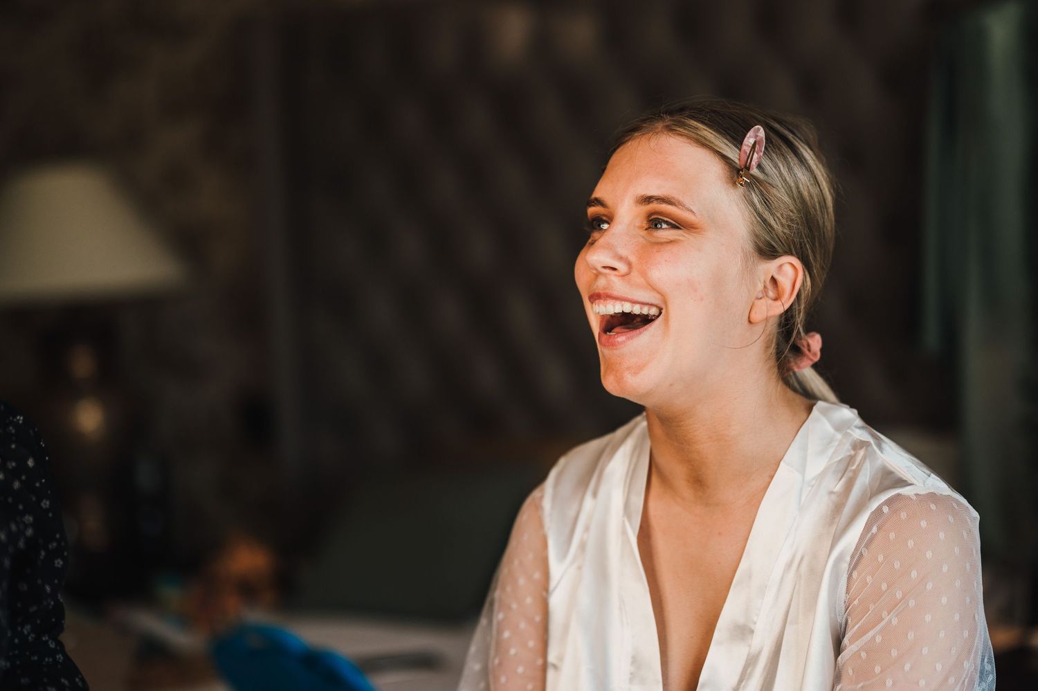 Woman in white blouse laughing joyfully during wedding preparations.