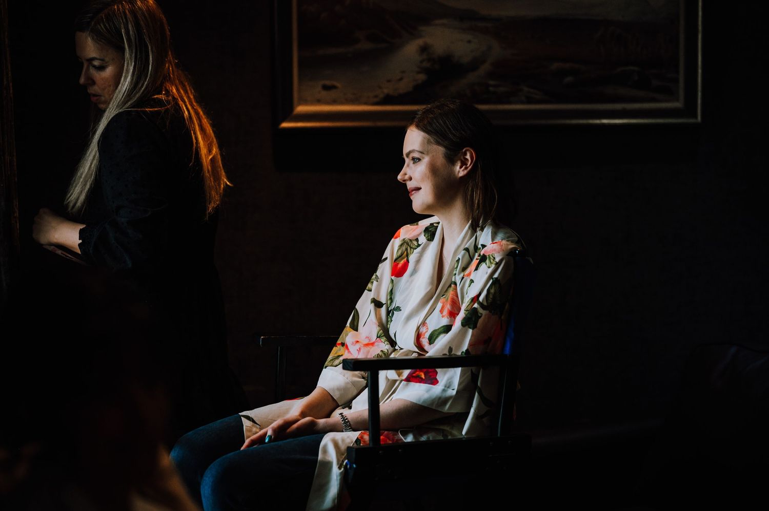 Person sitting in patterned dress illuminated by dramatic lighting in dark room.