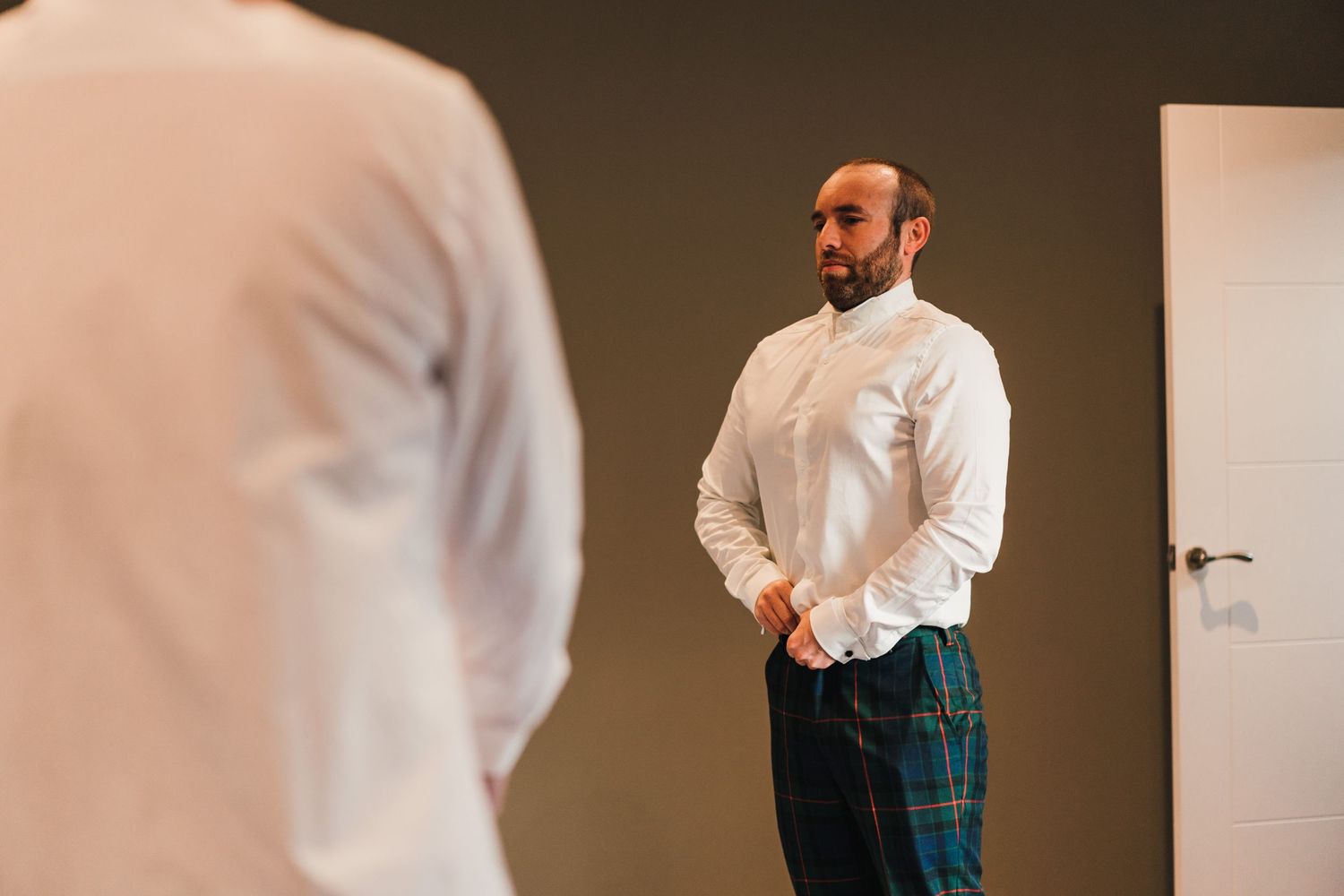 Gentleman wearing a white dress shirt and plaid pants standing in a modern hotel room.
