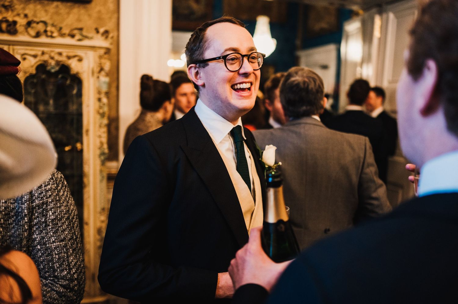 A guest laughs joyfully while holding a drink at an elegant indoor celebration.
