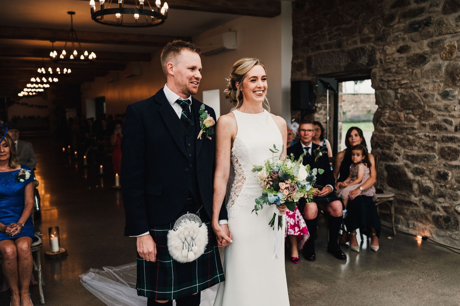 Newlyweds in Scottish wedding attire standing together during their ceremony.