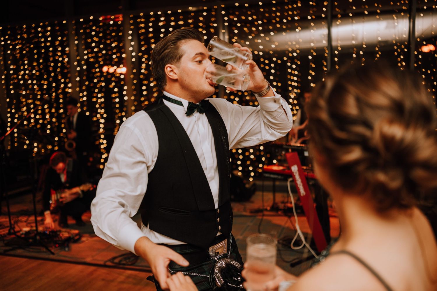 Reception guests dancing and celebrating at a wedding party with twinkle lights in the background.