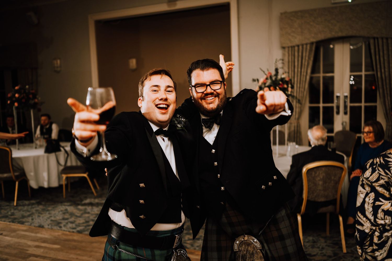 Two people in formal attire raise their drinks in celebration at a wedding reception.