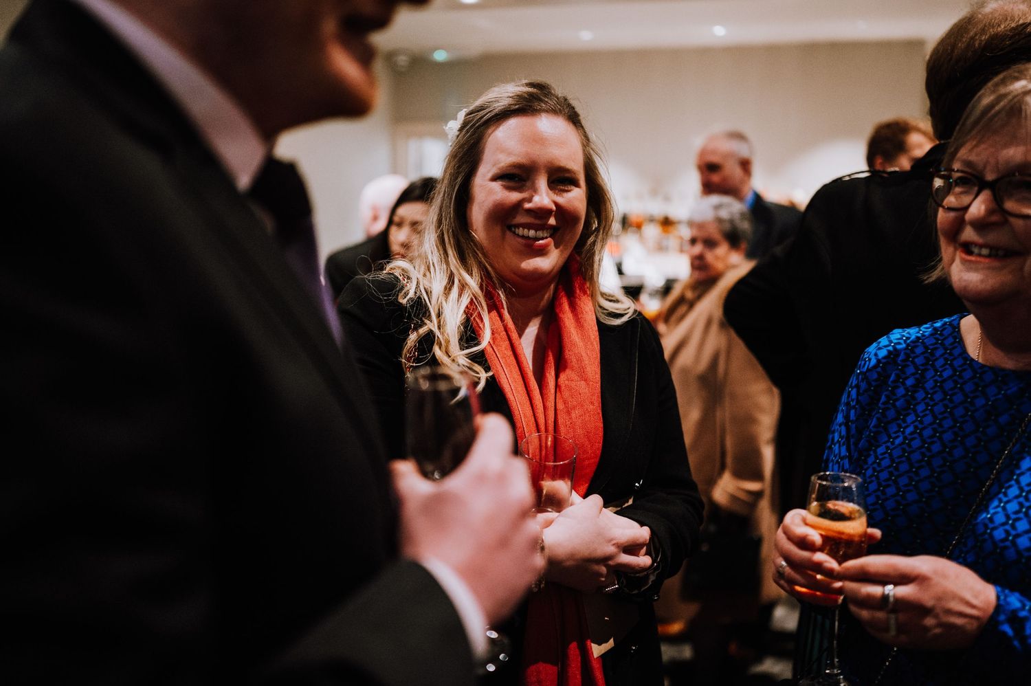 Wedding guests engaged in animated conversation during an indoor reception party.
