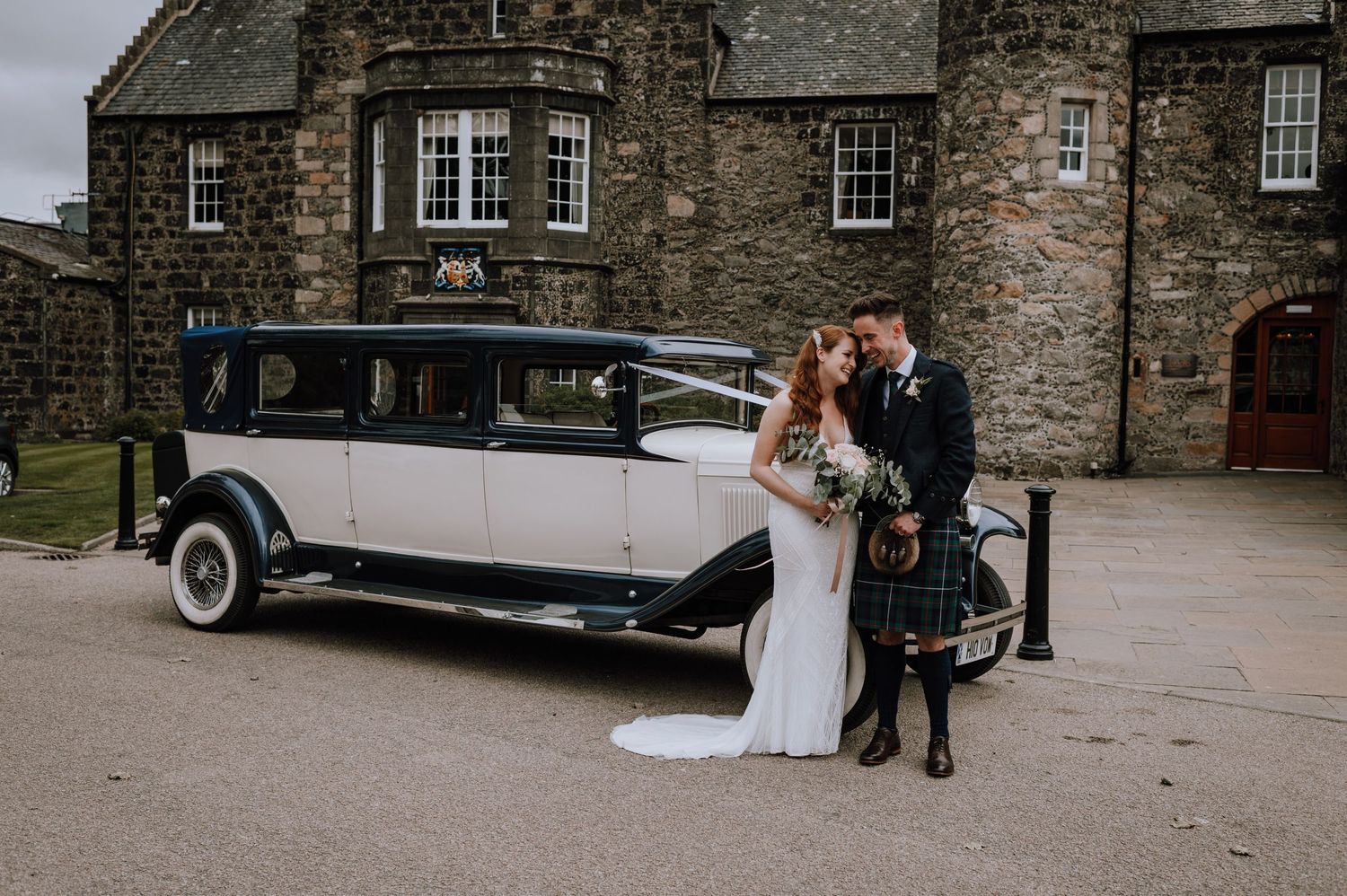 Vintage white wedding car displayed in front of historic stone building.