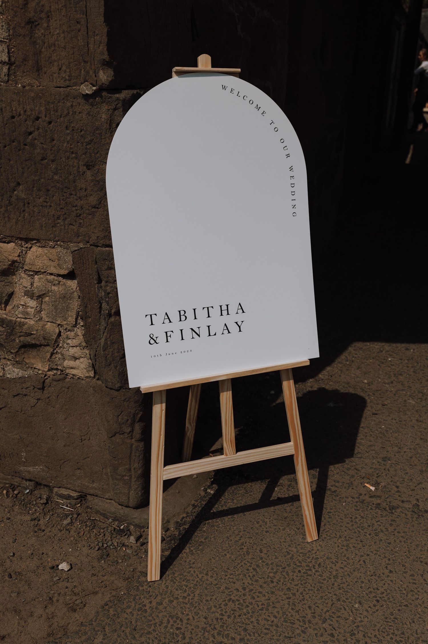 Elegant arched wedding welcome sign for Tabitha & Finlay displayed on wooden easel.