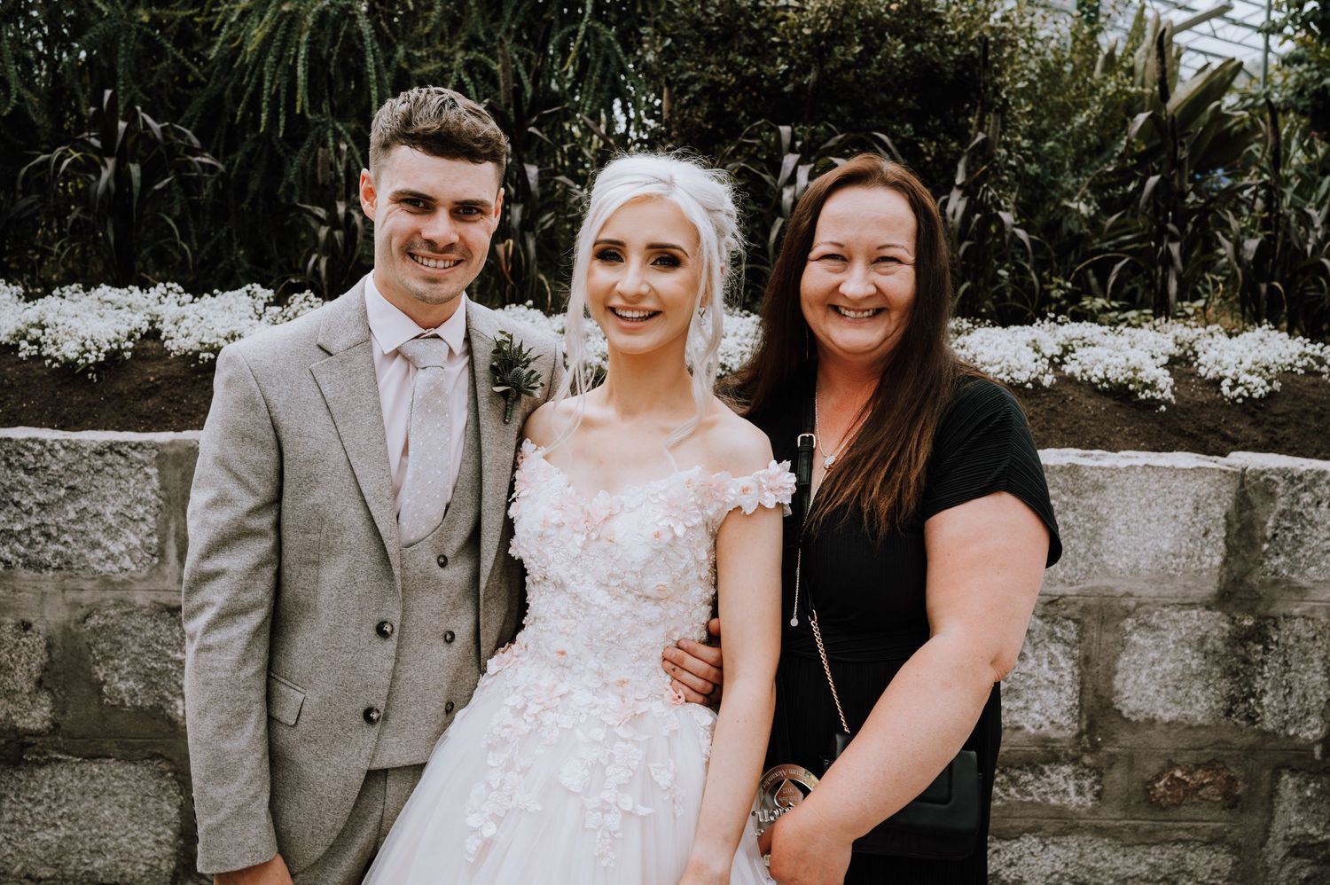A wedding portrait taken outdoors against a stone wall background.