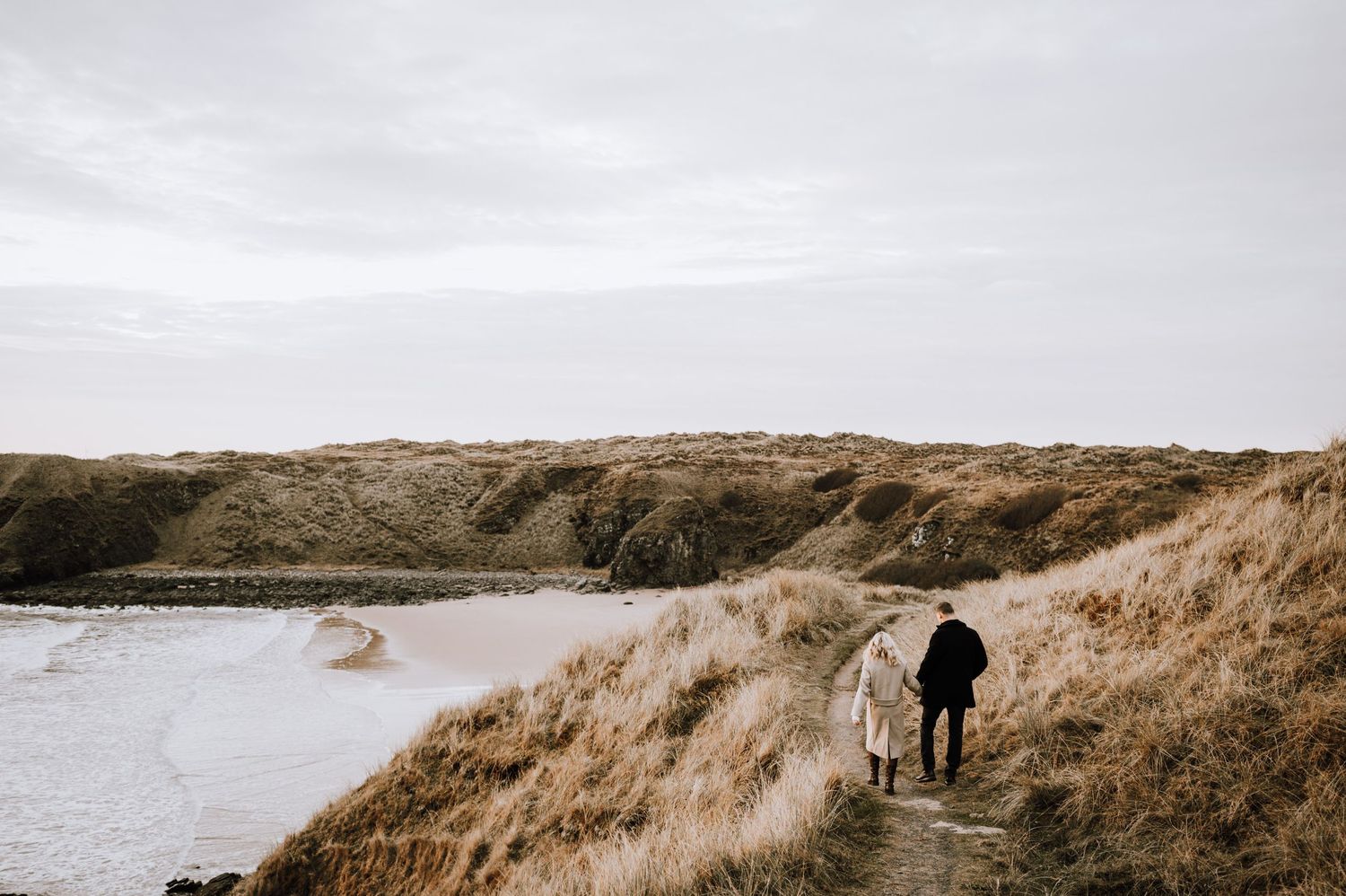 Two figures walking along a coastal path with dramatic cliffs and ocean views.