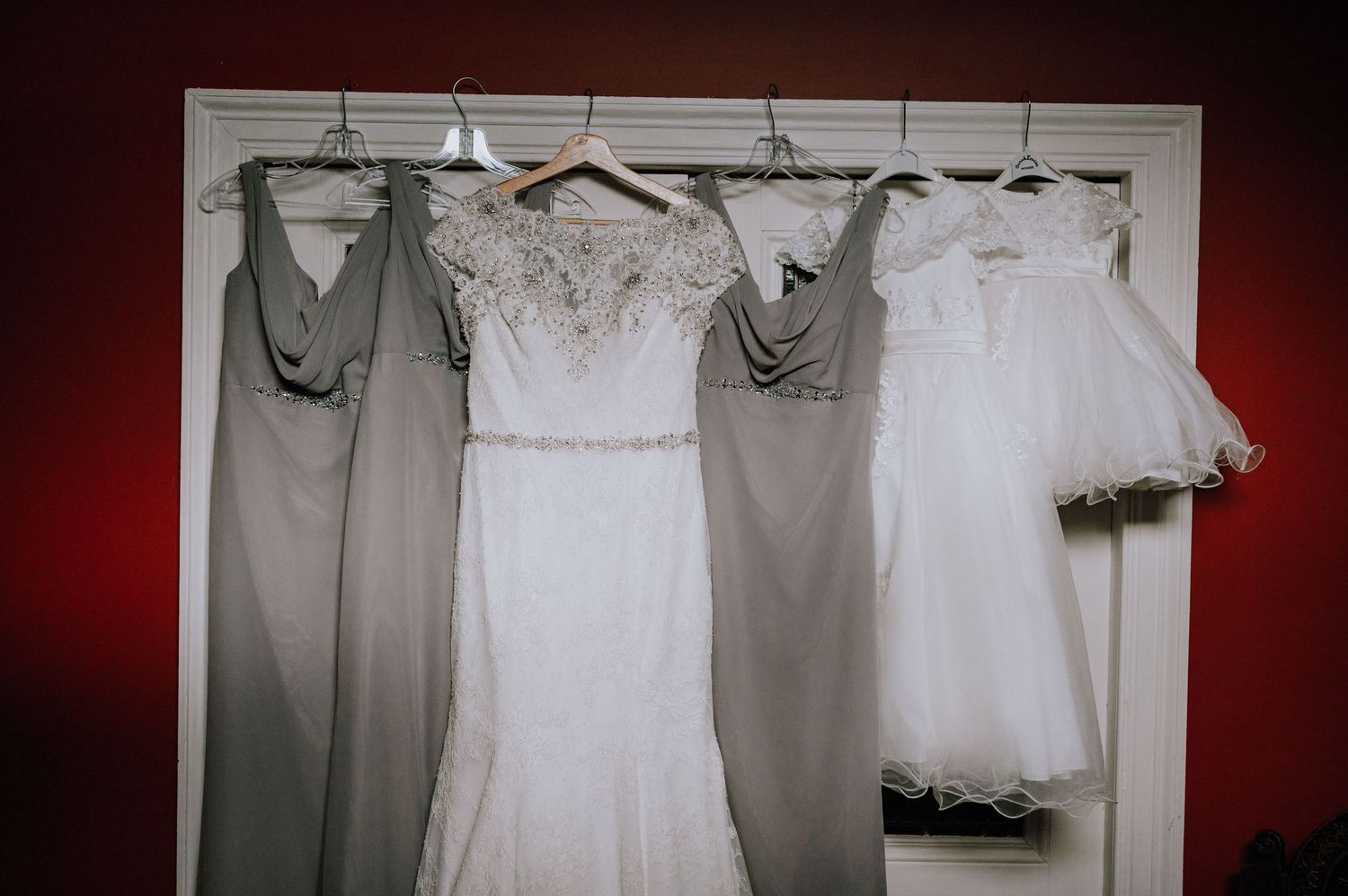 A white wedding dress hangs between gray bridesmaid dresses and a flower girl dress.