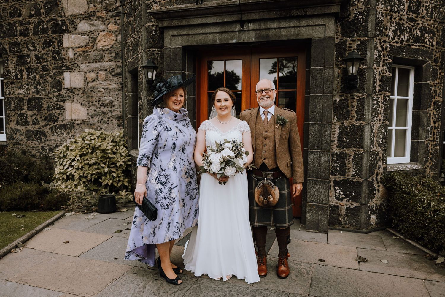 Traditional Scottish wedding portrait in front of a historic stone building entrance.