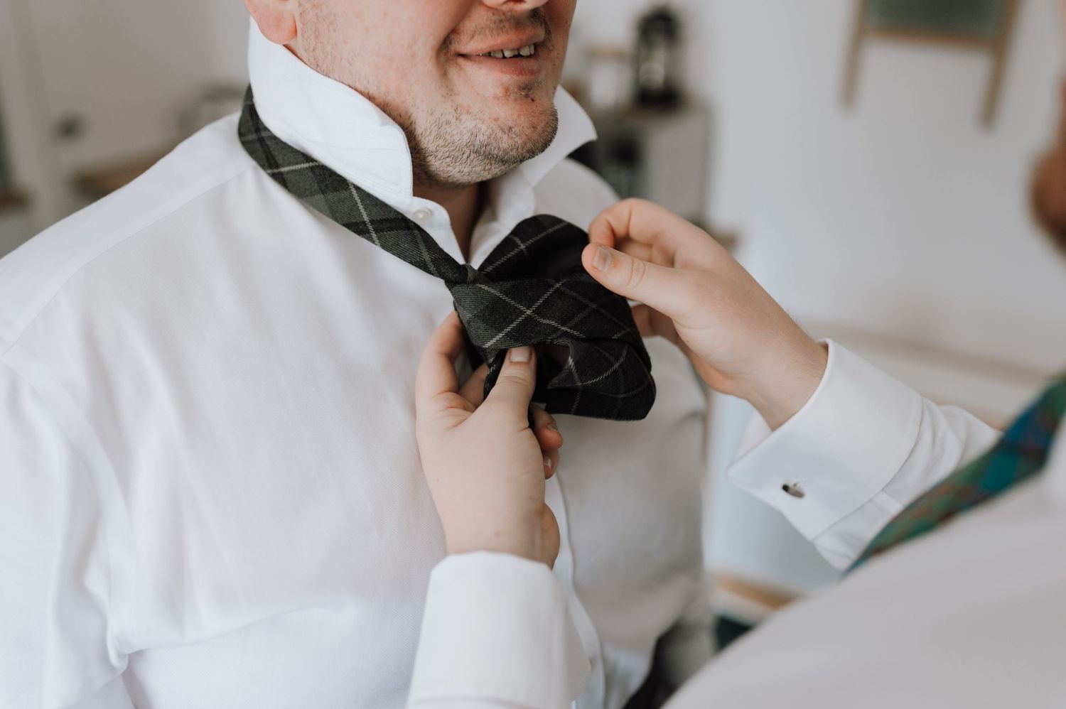 Close-up of hands tying black bow tie on white formal shirt.