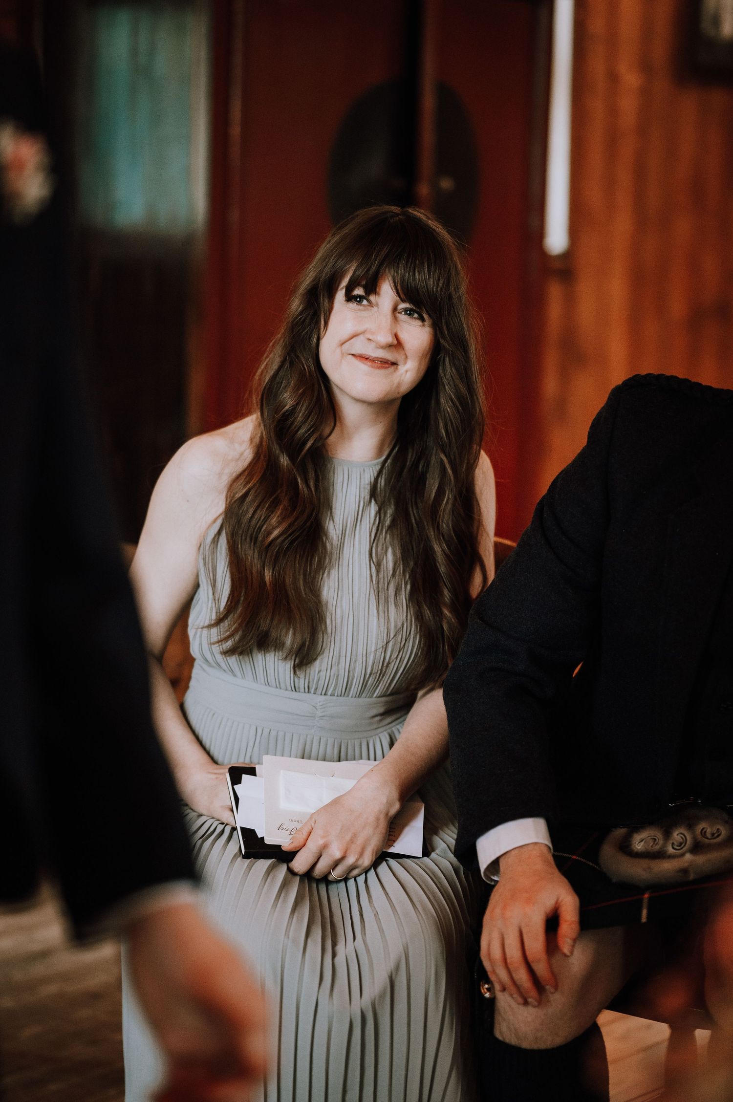 A guest in a gray pleated dress at a rustic wedding venue with wooden walls.