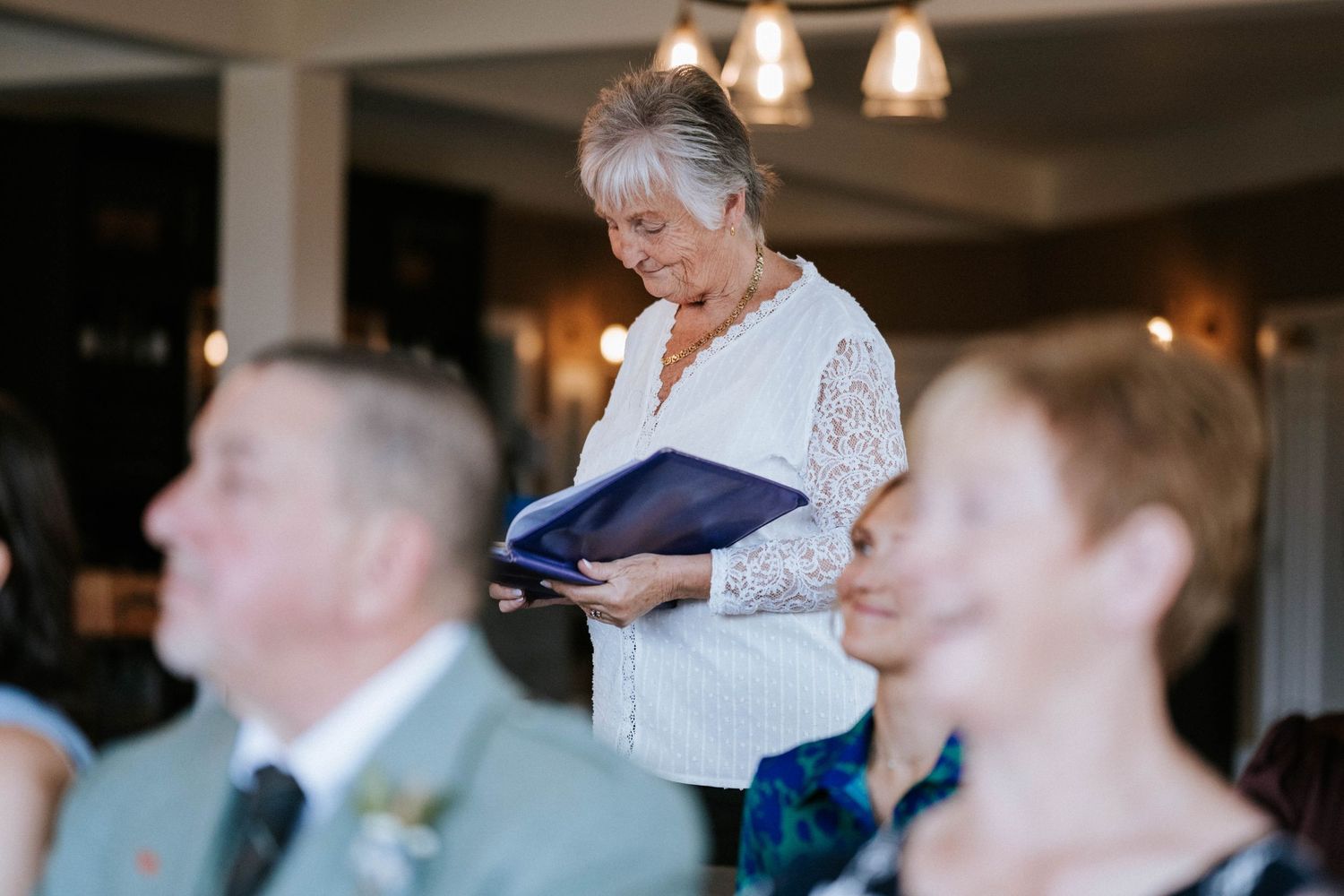 A group of wedding guests listen attentively during a reception speech in an elegant indoor venue.