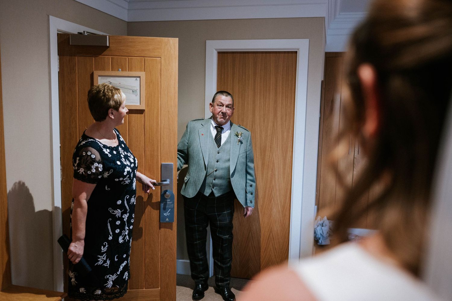 A wedding day first look moment in a hallway with wooden doors and white trim.