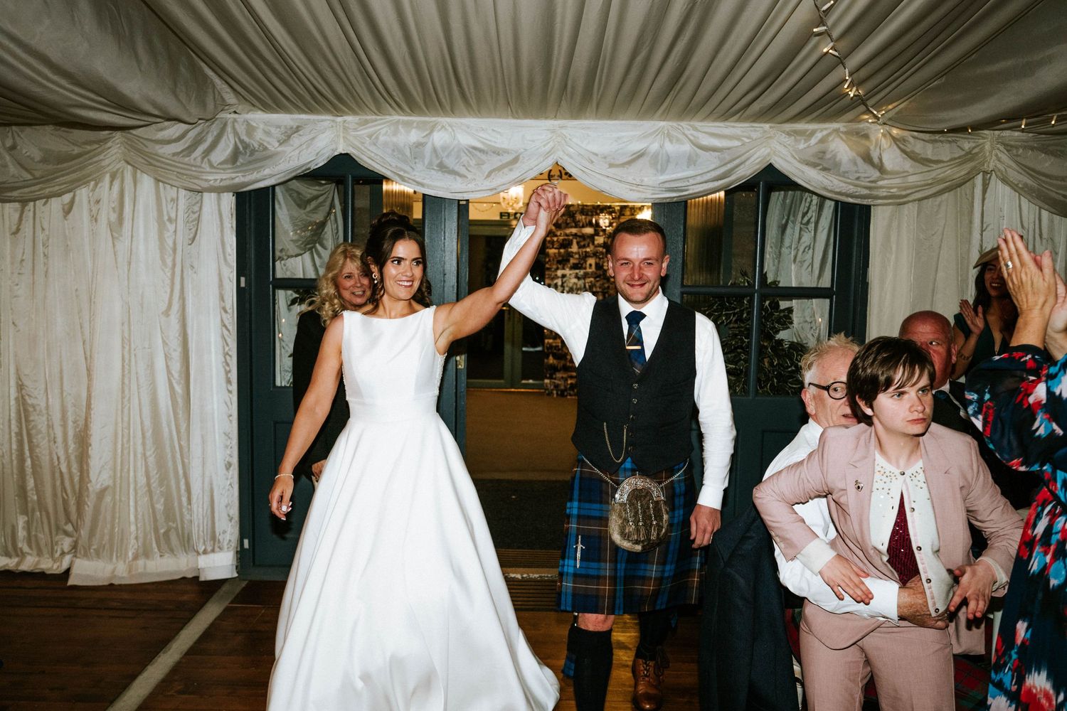 Wedding party dancing and celebrating inside a white tent reception venue.