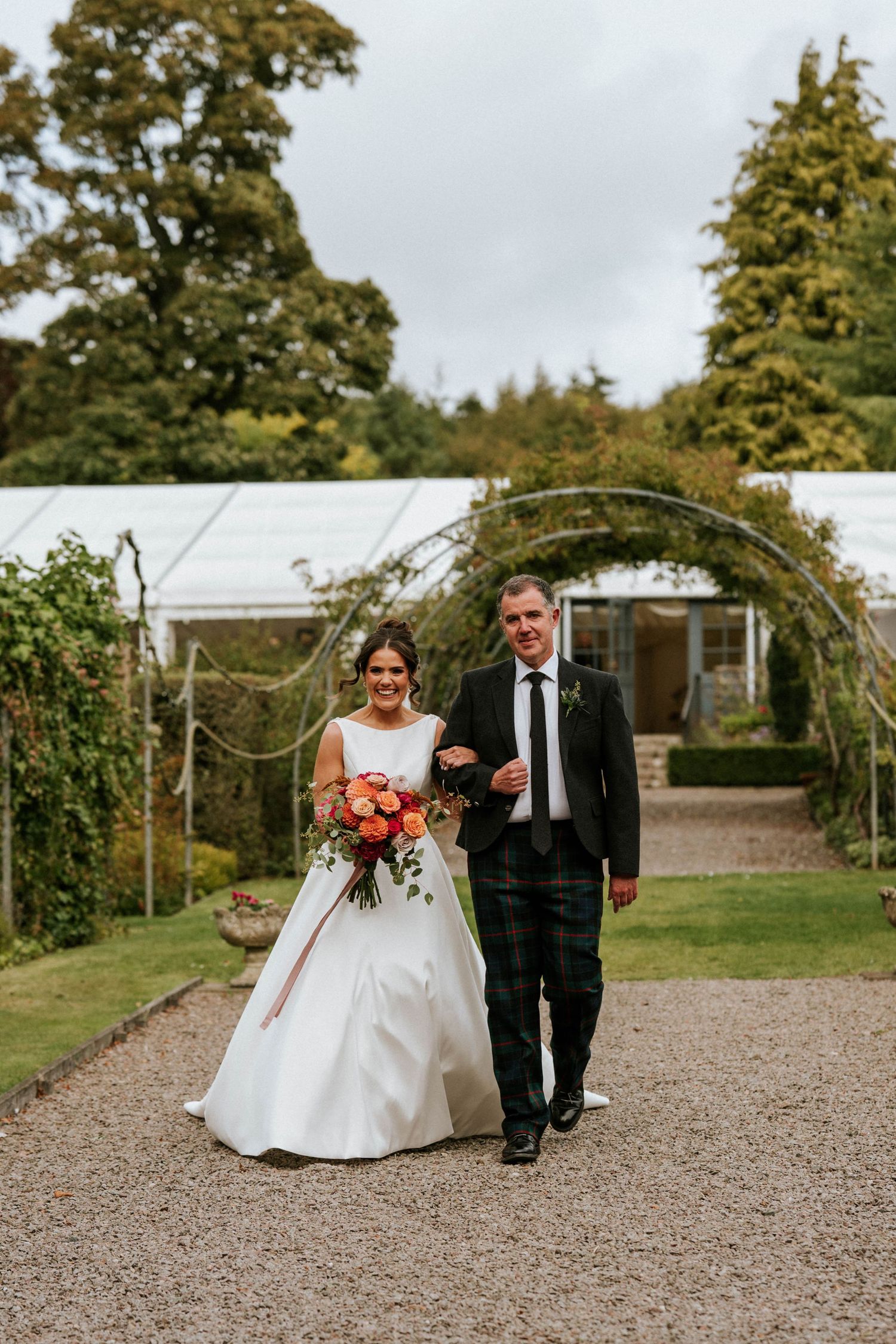 Couple walking together on a gravel path in front of a stately building.