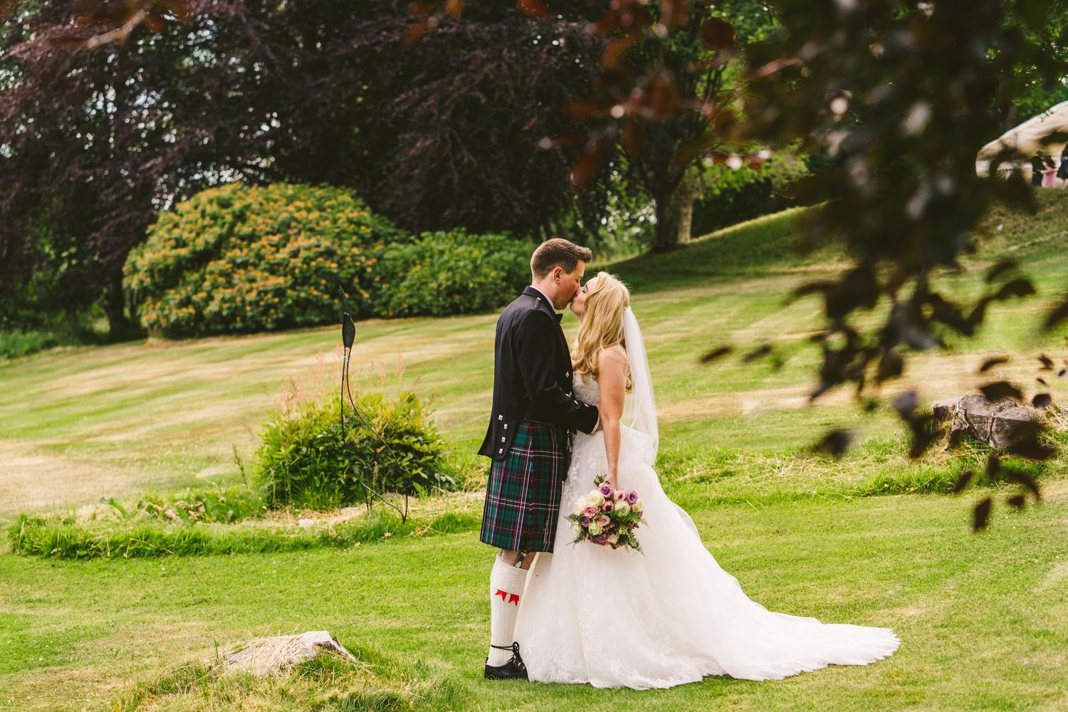 Wedding party posing on landscaped grounds with stone building in background.