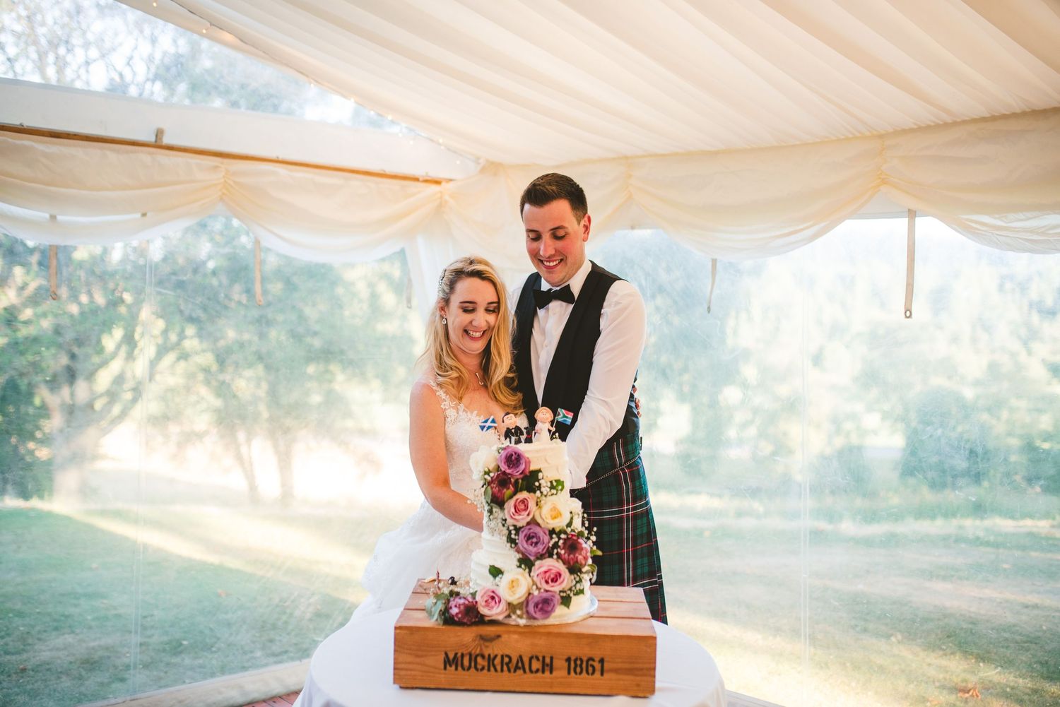 Wedding party celebrates under elegant white tent with bright natural lighting and festive decor.
