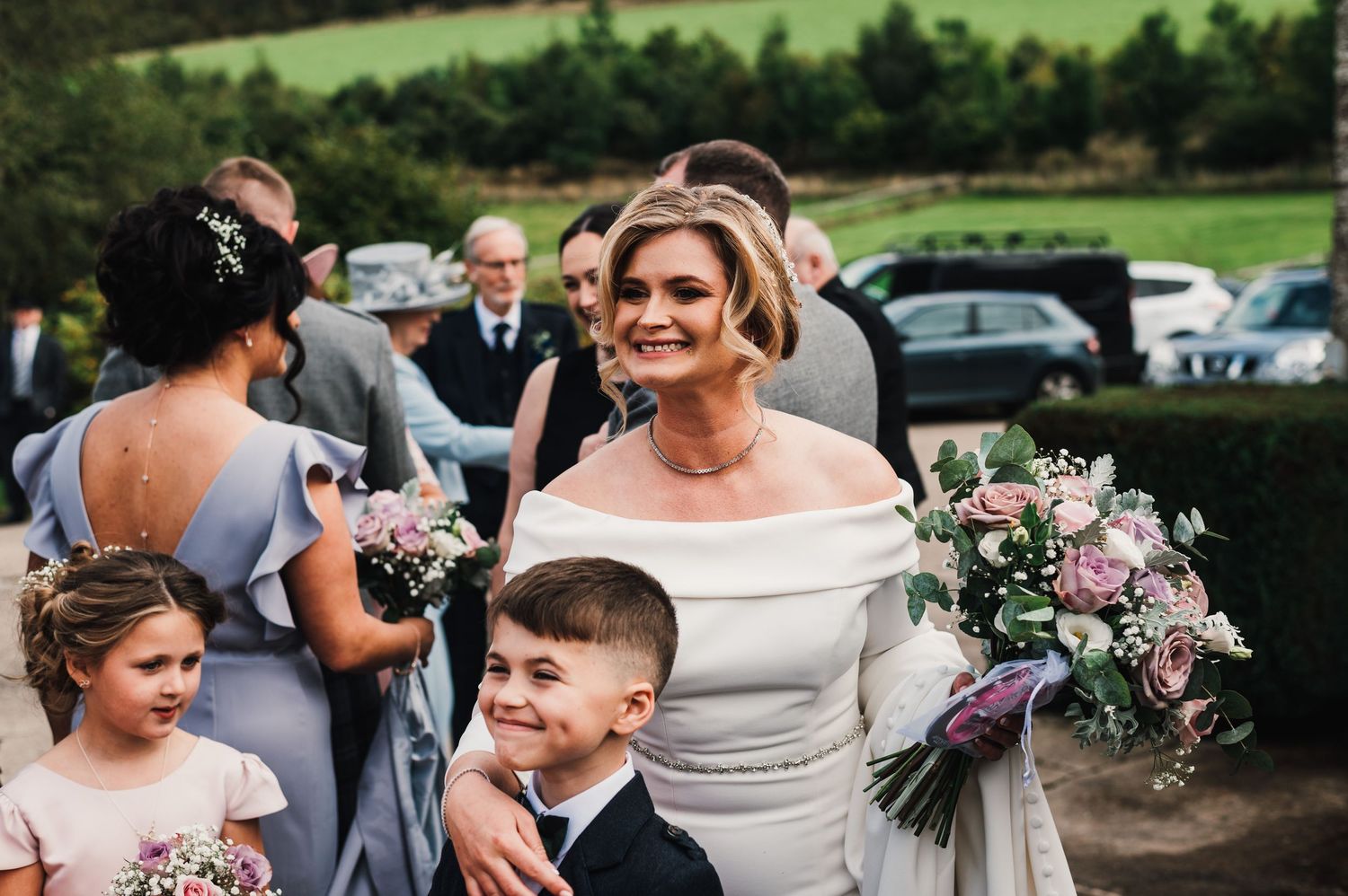 Wedding party gathered outdoors with pink floral bouquets and grey attire.