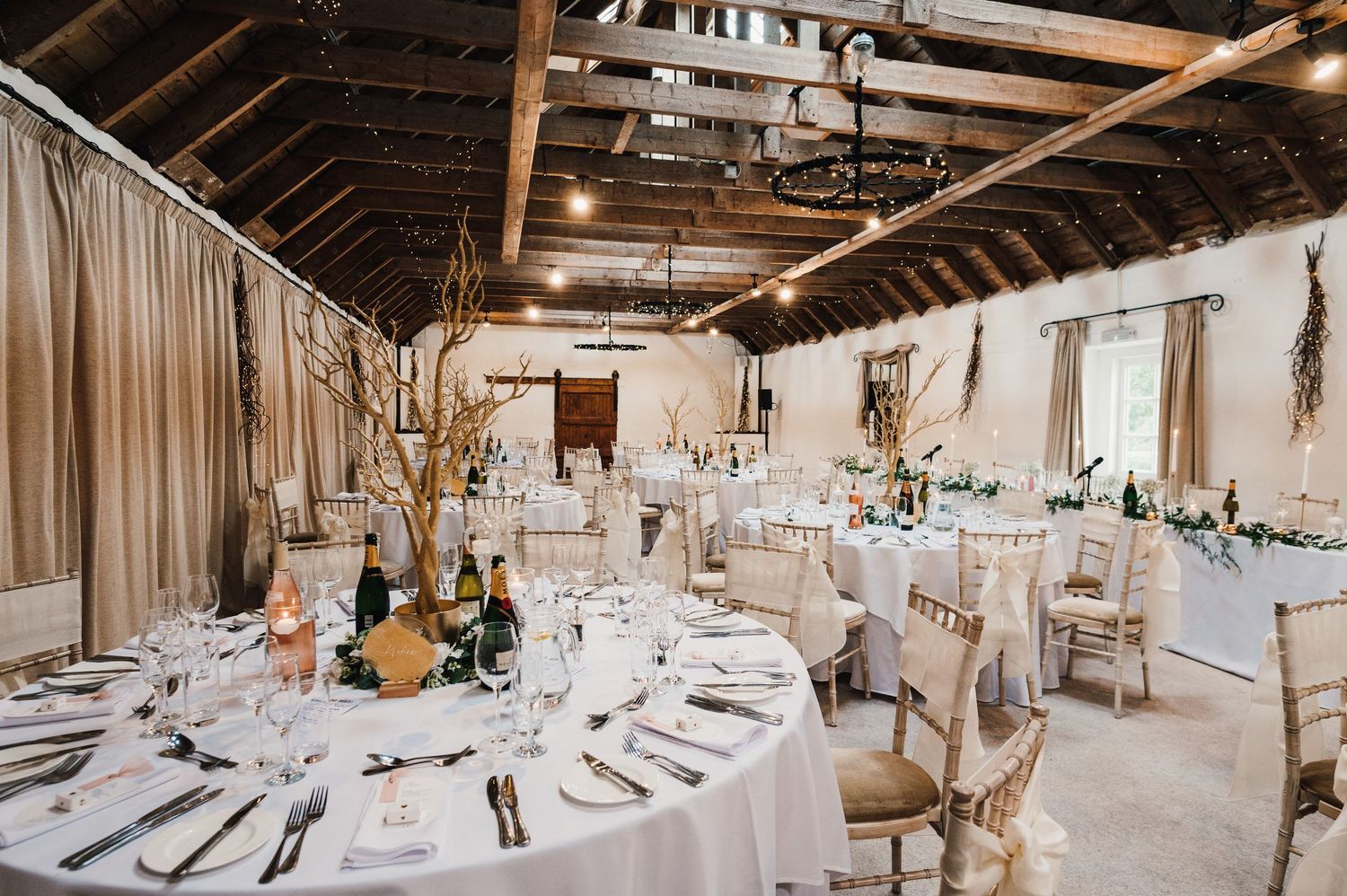 Rustic barn wedding reception setup with long tables and white draping decor.