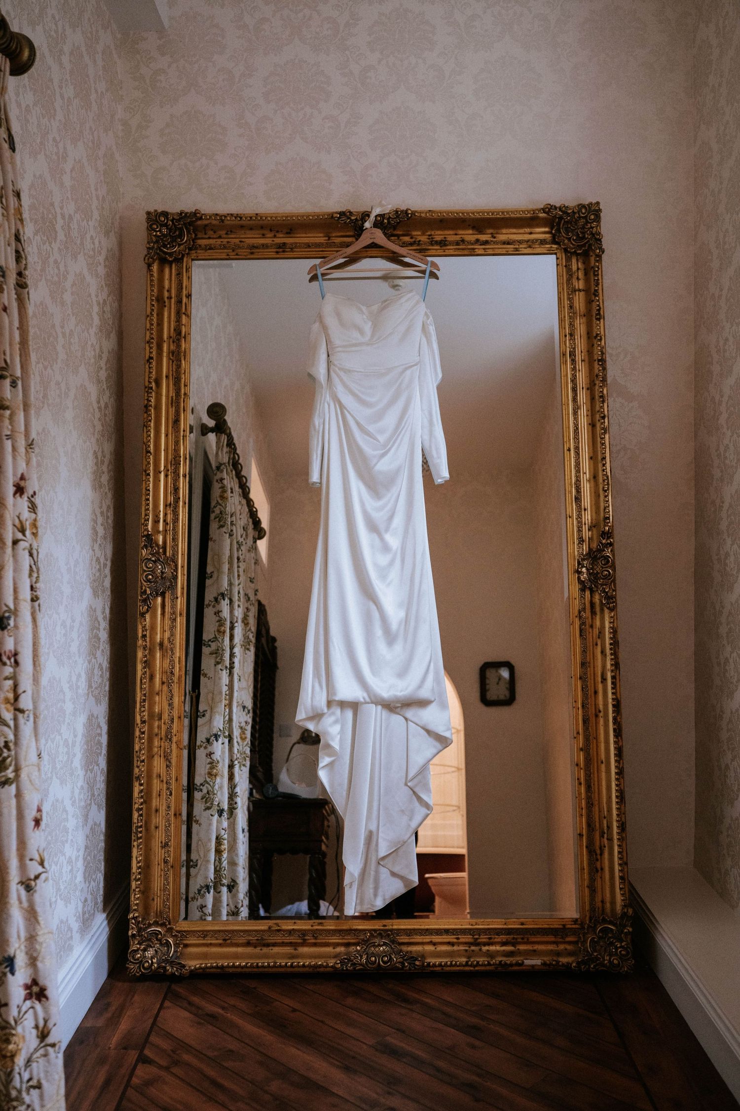 Series of white wedding dresses hanging on display against a wall with ornate gold-framed mirrors.