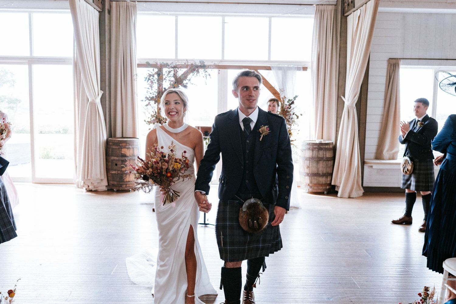 Light-filled wedding venue with white drapes and guests mingling before the ceremony.